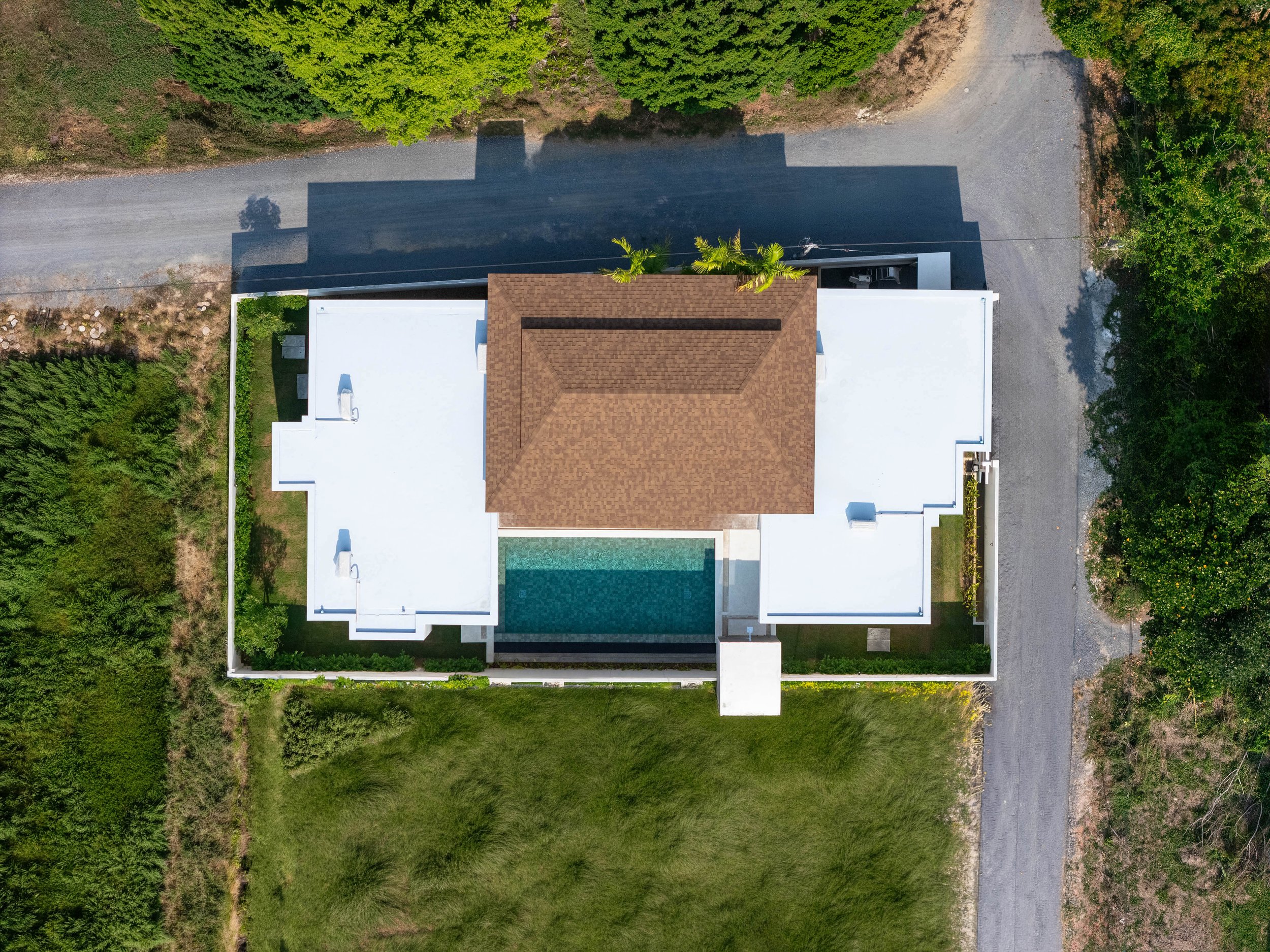 Luftaufnahme eines modernen Hauses mit grünem Garten, Pool und umliegender Natur.