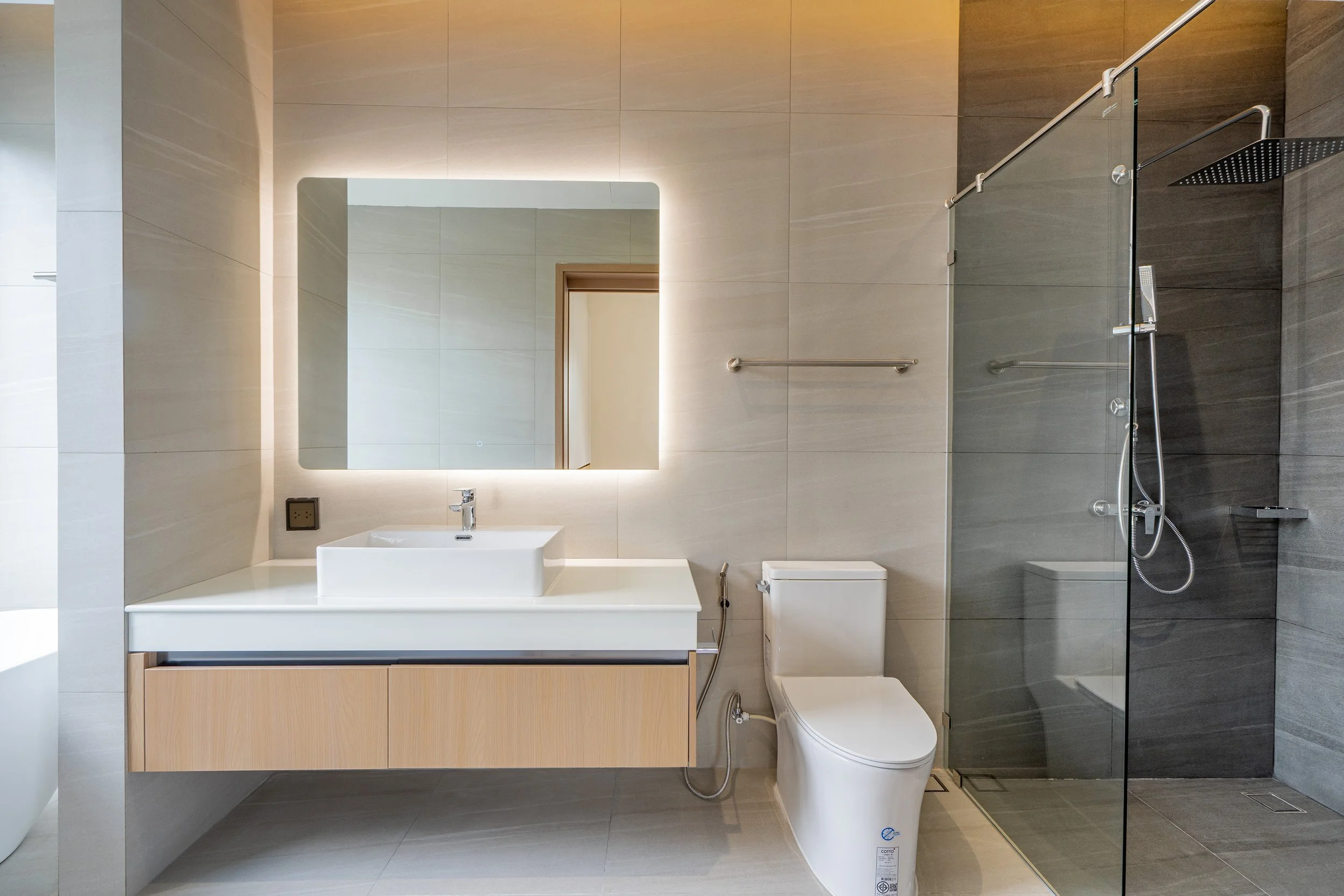 Modernes Badezimmer mit großem Spiegel, Waschbecken, Toilette, ebenerdiger Dusche mit Glasscheibe und Handtuchhalter, hellem Wand- und Bodenfliesen.