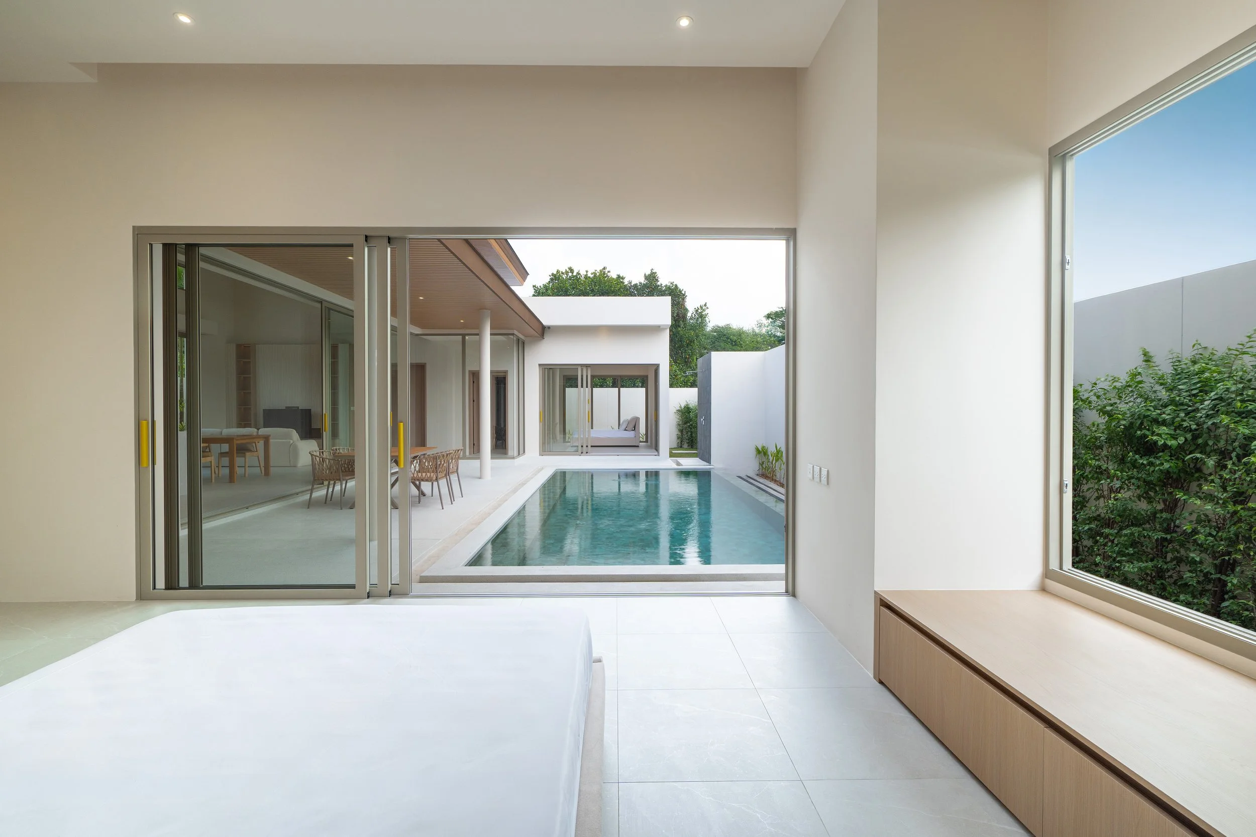Moderner Innenraum mit Blick auf einen Swimminpool, große Fenster, helle Wände und minimalistisches Mobiliar.