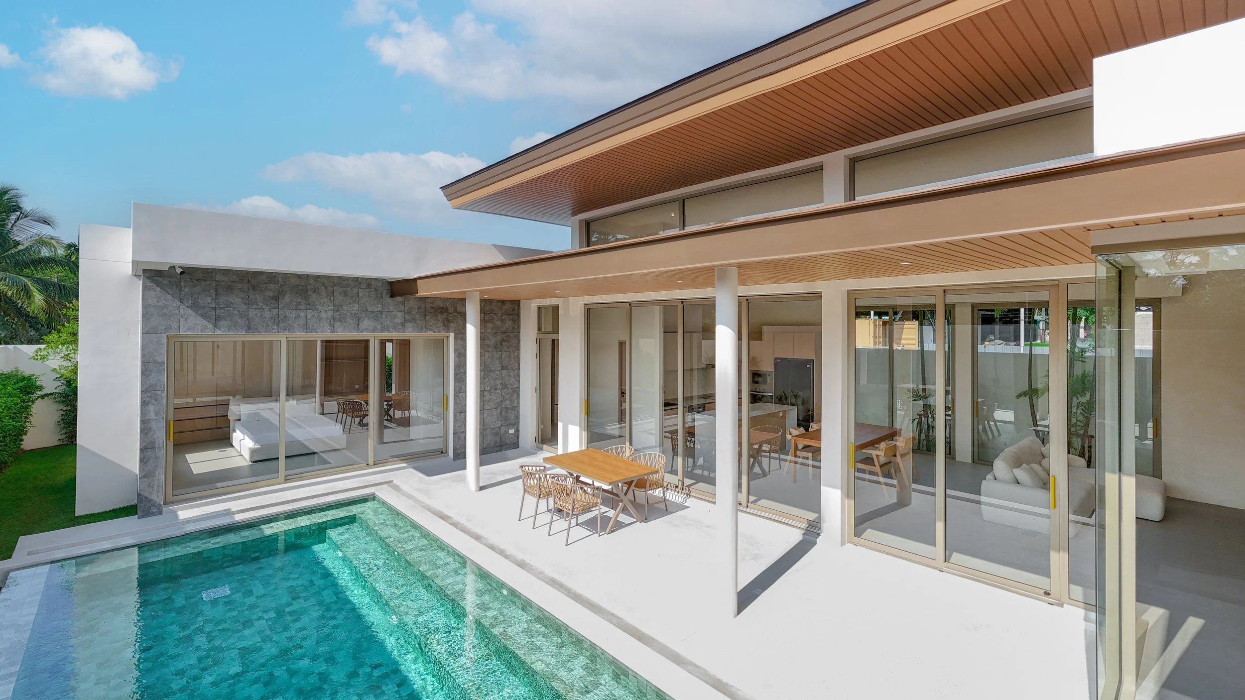 Modernes Haus mit Glasfenstern und Sicht auf den Pool und den Garten, inklusive Sitzbereich mit Tischen und Stühlen im Außenbereich.