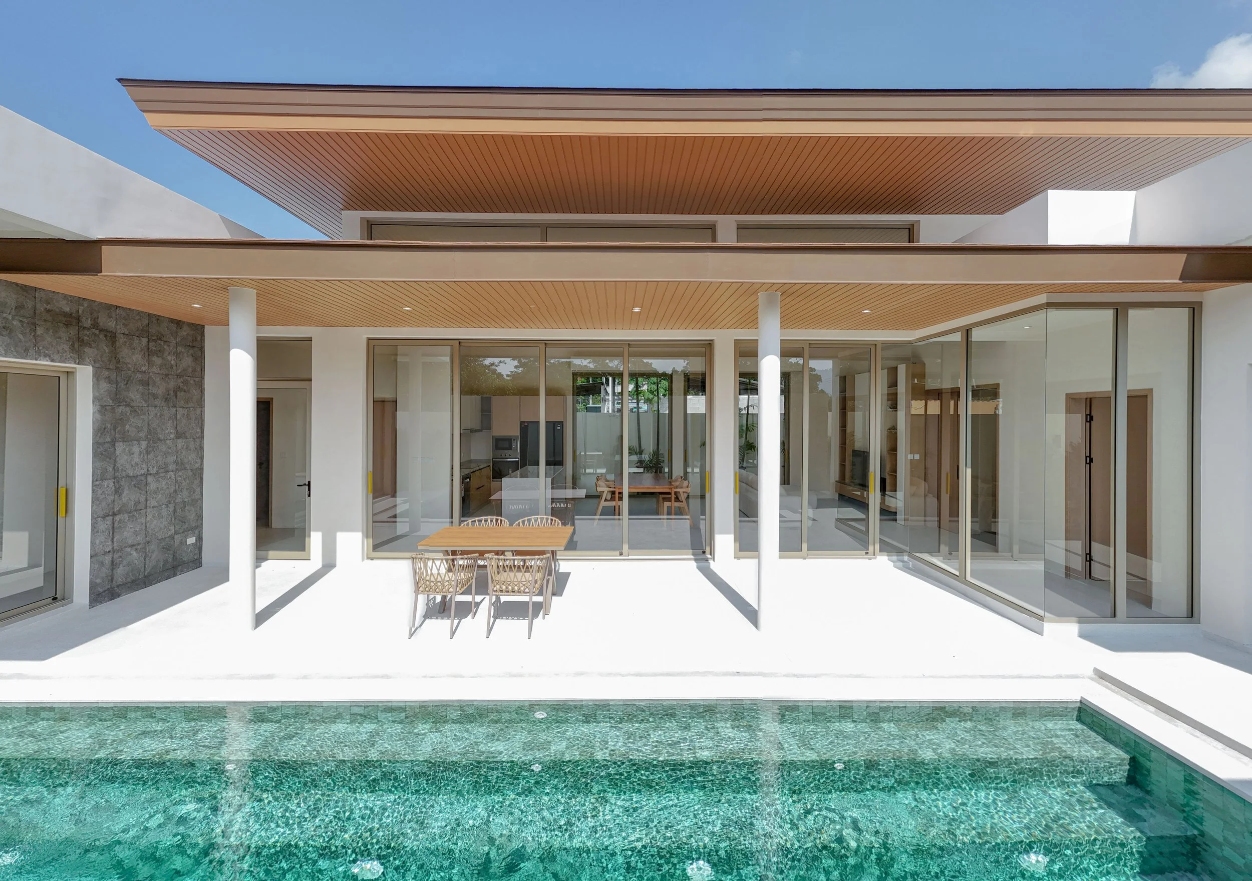 Modernes Haus mit einem Pool im Vordergrund, große Glasfenster, Holzverkleidung an den Decken, weißer Außenwand.