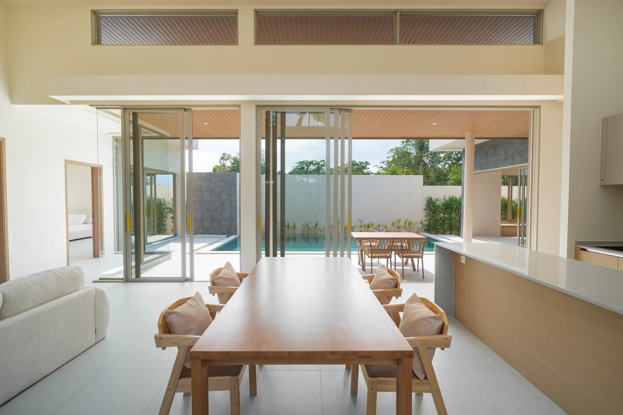 Innenansicht eines modernen Wohnzimmers mit Blick auf einen Außenpool und Garten, großer Esstisch aus Holz, moderne Architektur, viel Glas und natürliche Materialien.