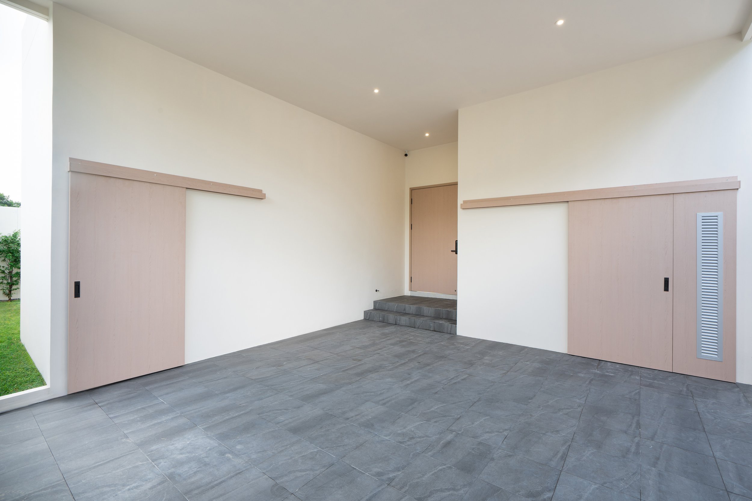 Moderner Eingangsbereich mit grauen Fliesen, weißen Wänden, einer Tür, Treppe und versteckten Schiebetüren aus Holz.