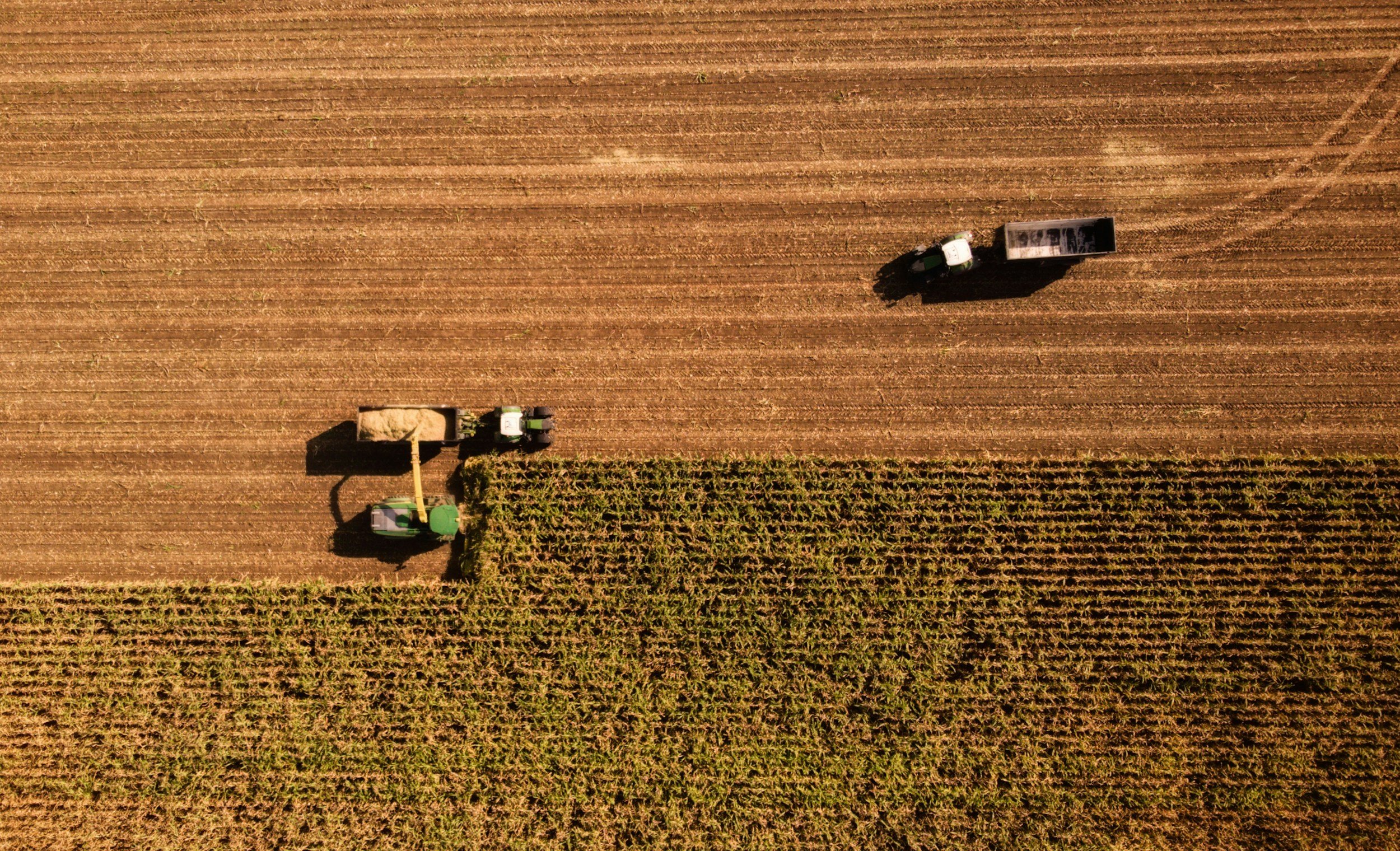 Aerial view of tractors working on a large agricultural field, planting or harvesting crops during daylight.
