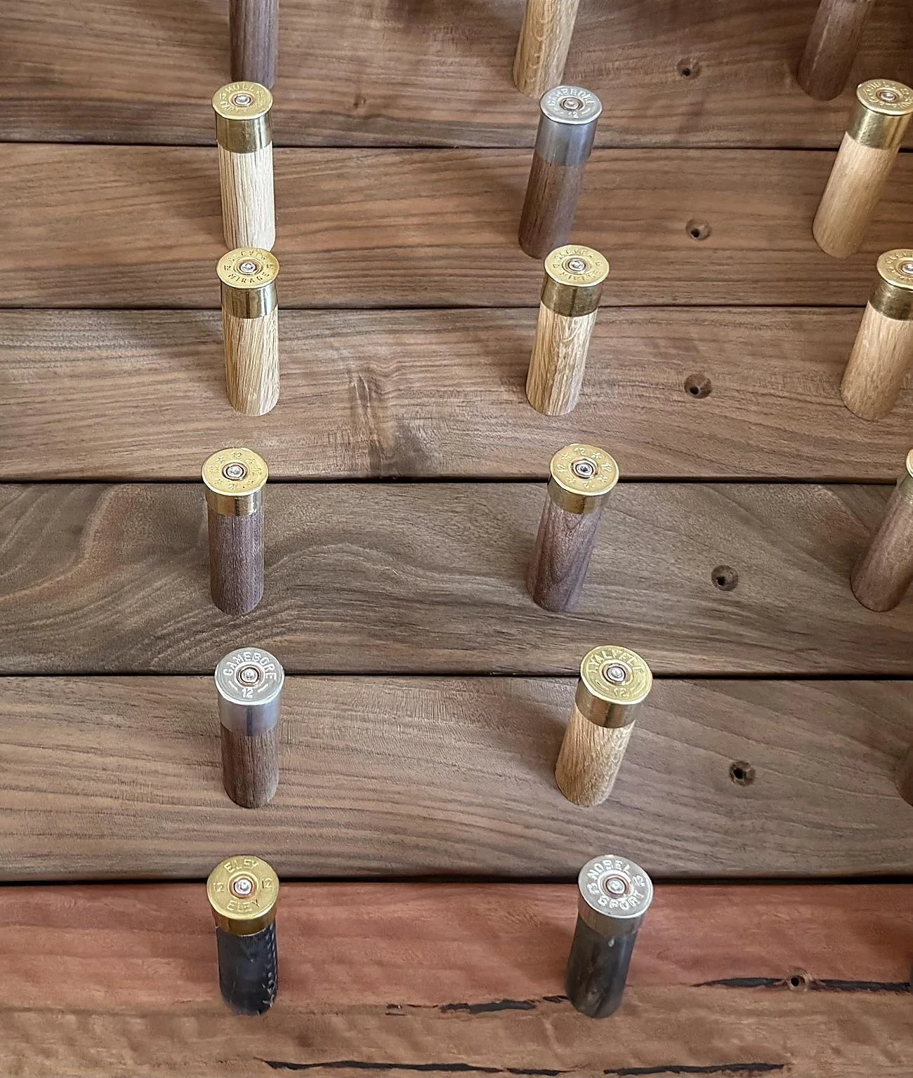 Close-up of a wooden surface with scattered shotgun shells of various colors and brands, some upright and some lying down.