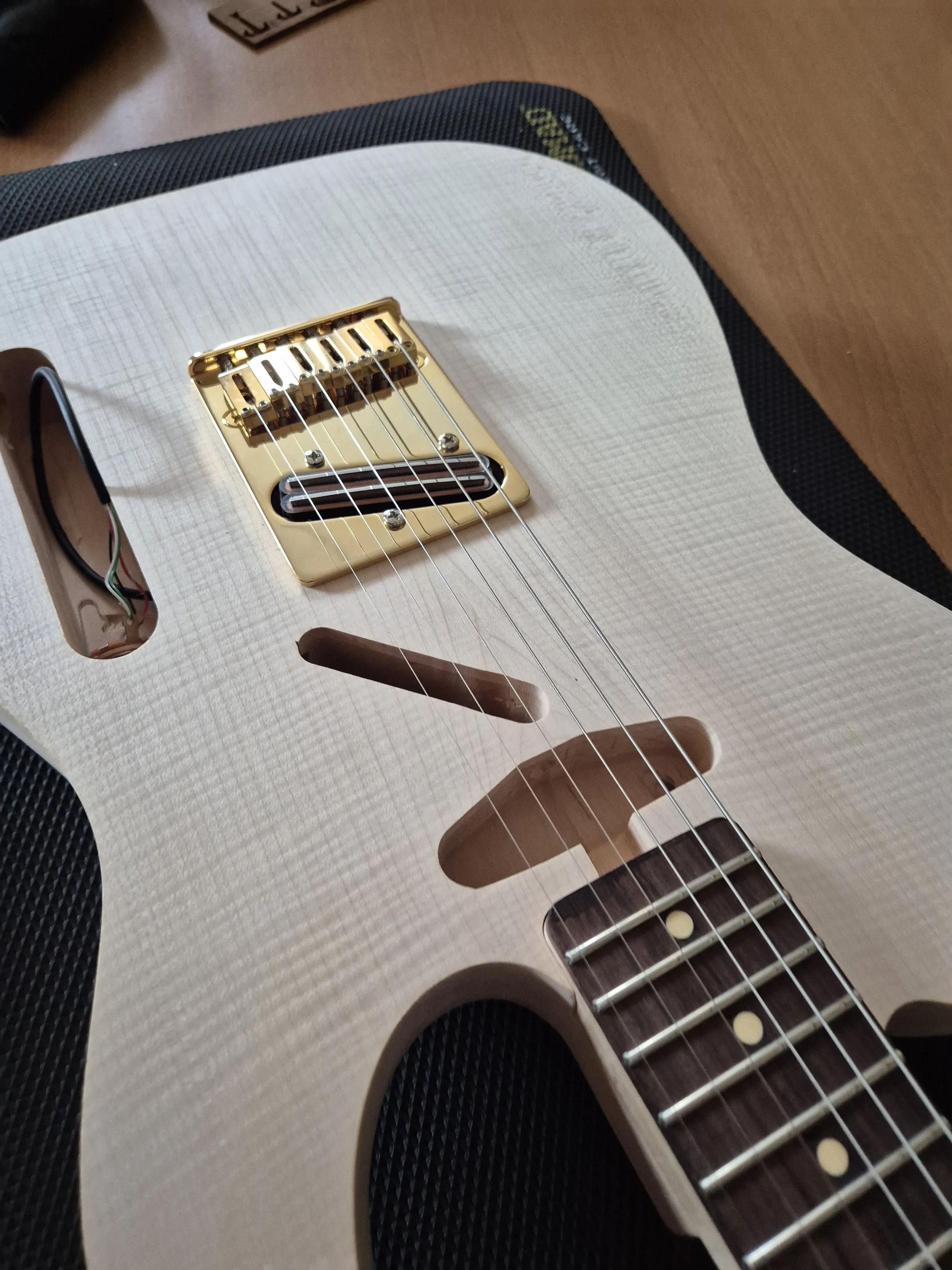 Guitare électrique blanche avec des cordes, un chevalet en or et une touche en bois foncé, posé sur une surface en bois.