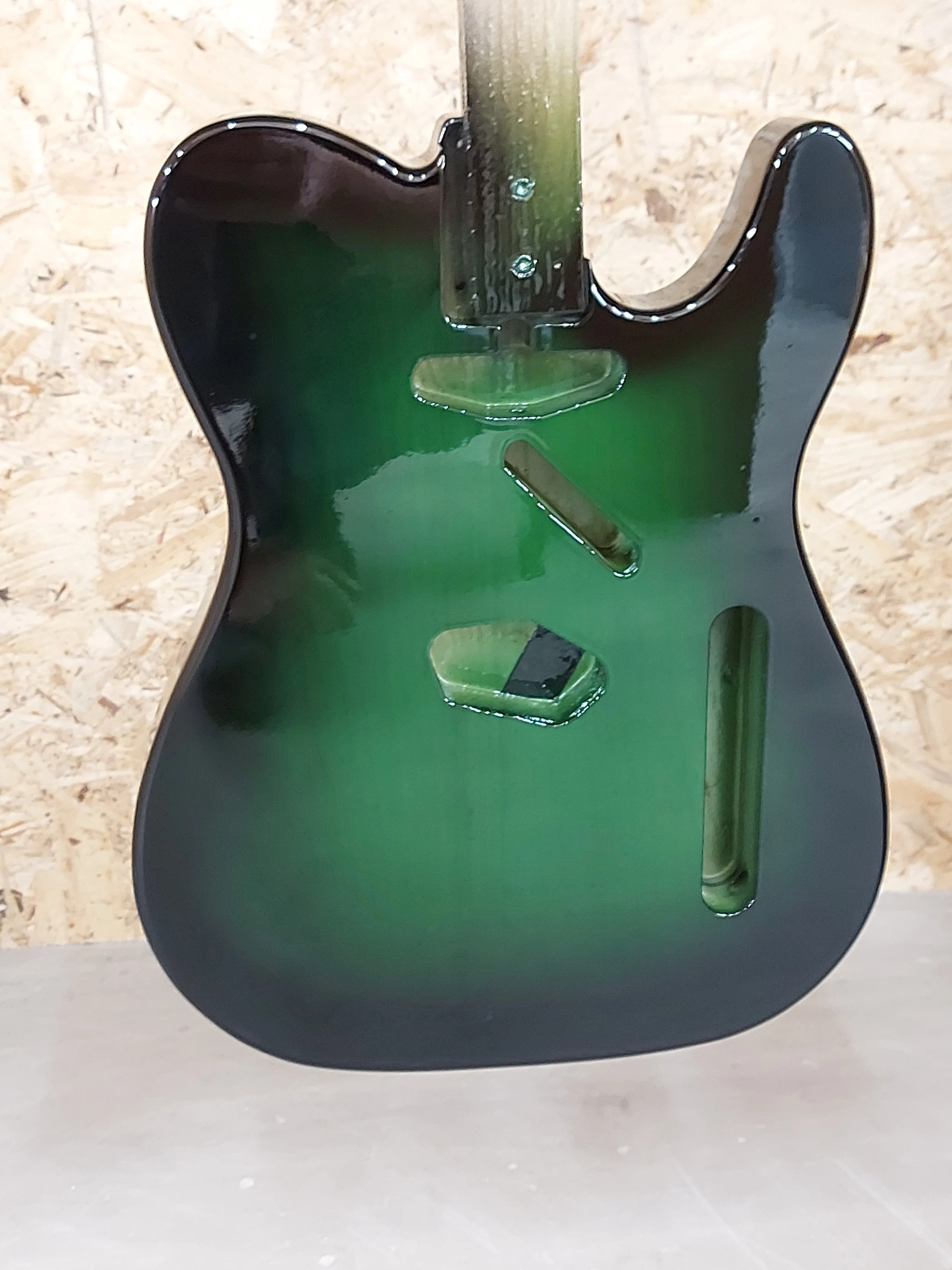 Une guitare électrique de couleur noire avec un dégradé vert, vue de dessous, posée sur un fond en bois.