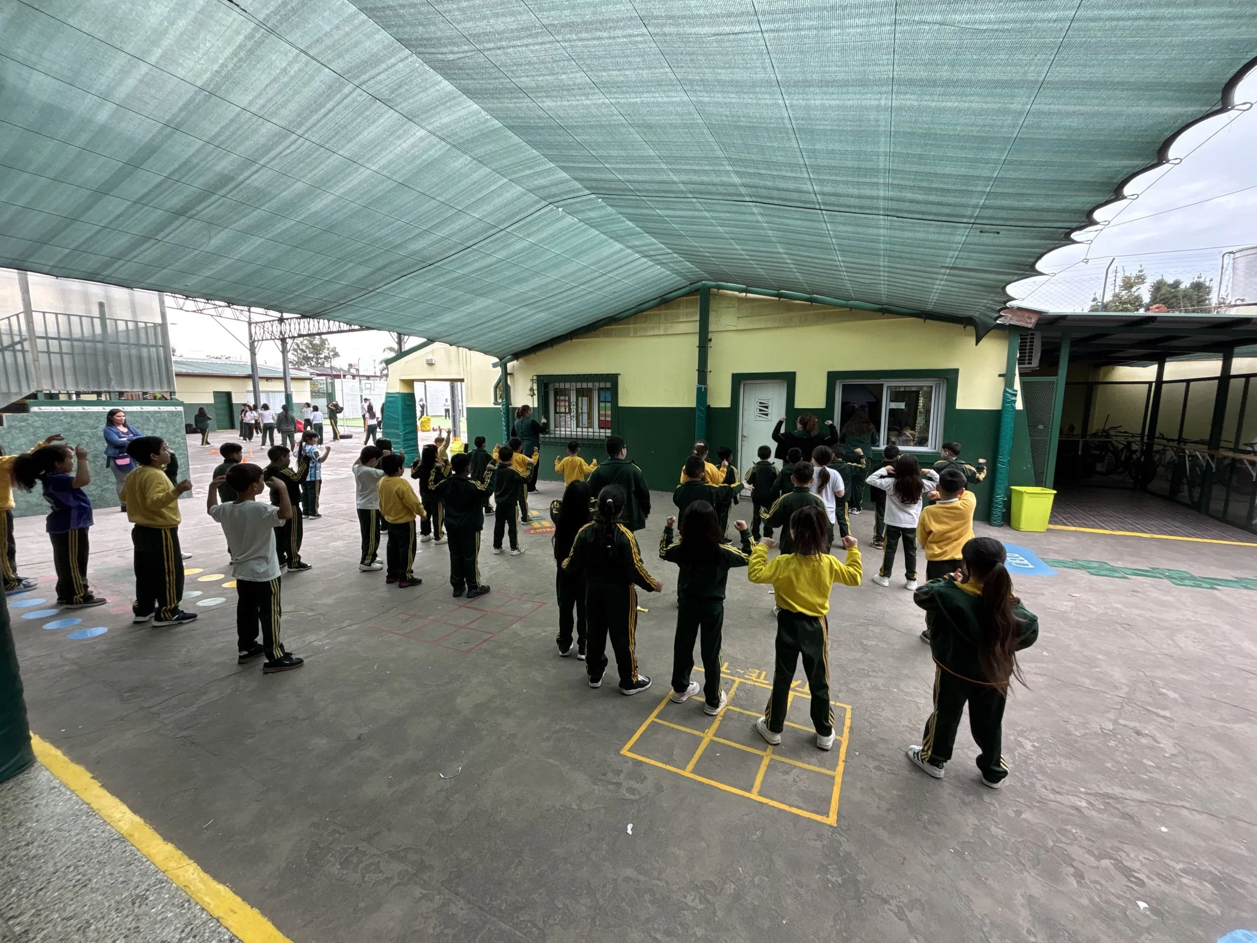 Estudiantes realizando una actividad recreativa y ejercicios al aire libre en el patio techado del colegio.