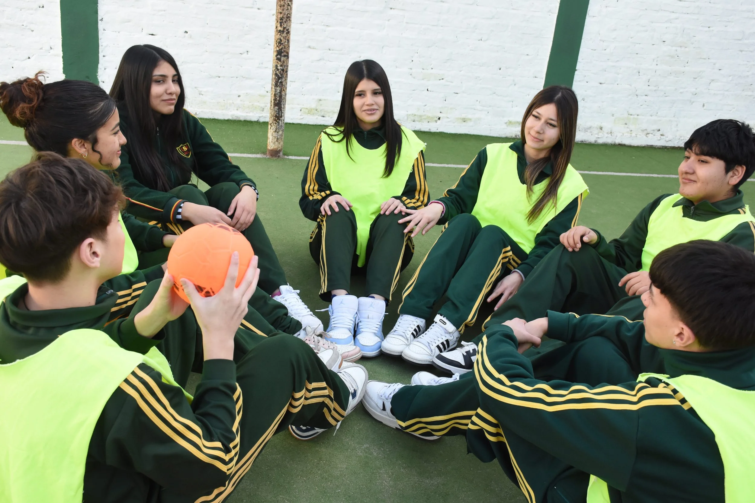 Estudiantes de secundaria participando en una actividad grupal con una pelota en el patio de deportes de la escuela.