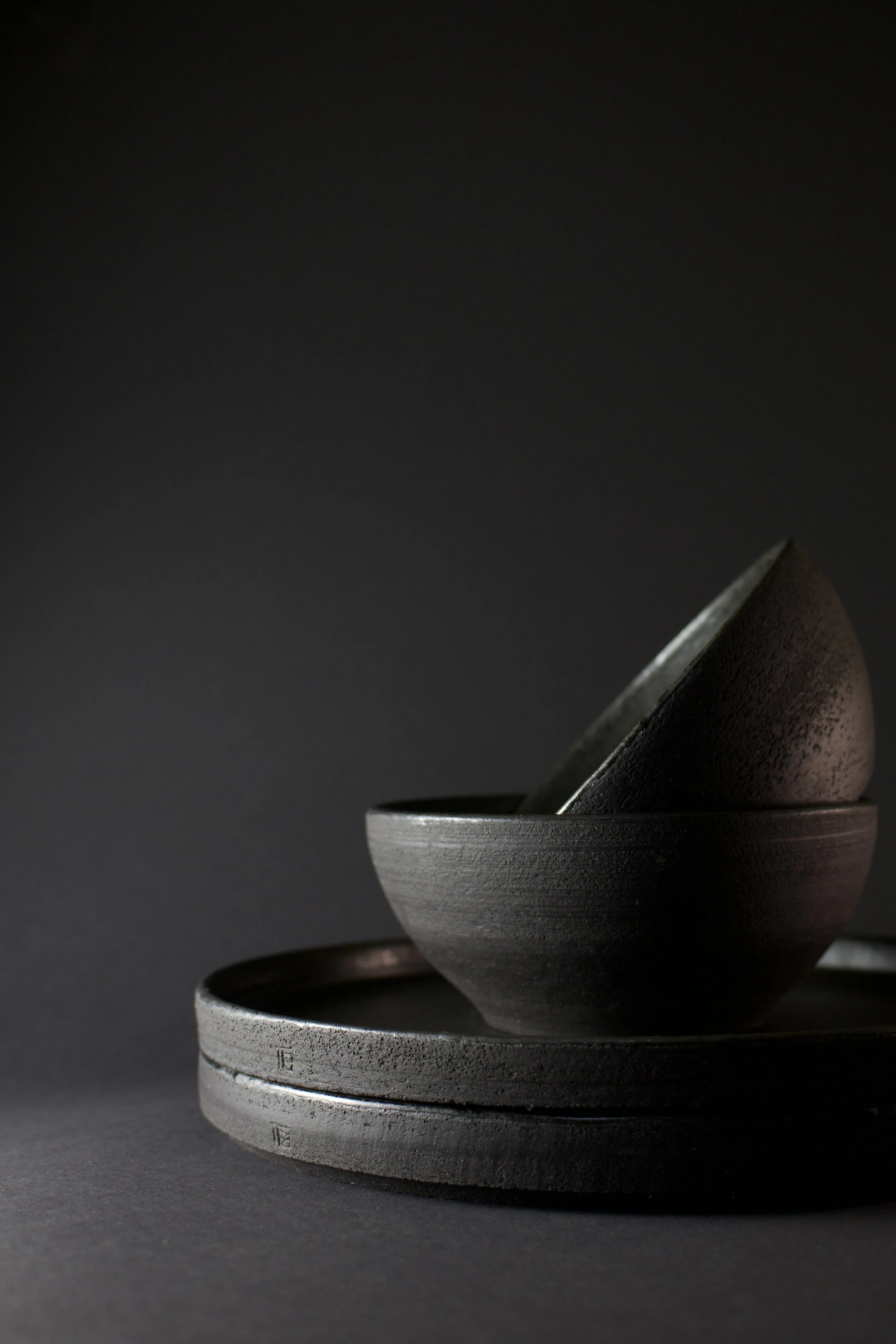 Stacked black ceramic bowls with a rough matte finish on a dark background.
