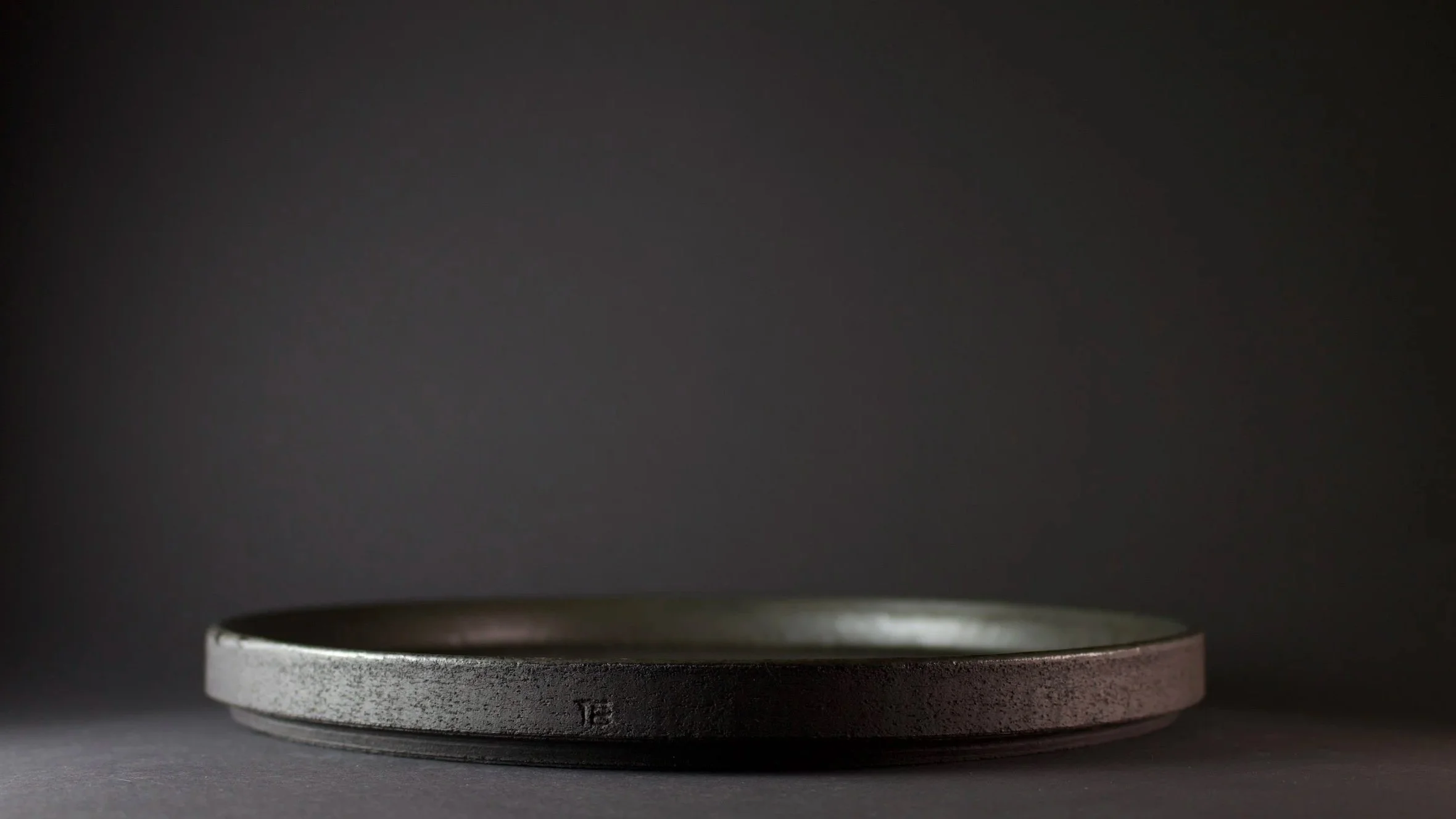 A close-up of a handmade stoneware plate, against a dark background.