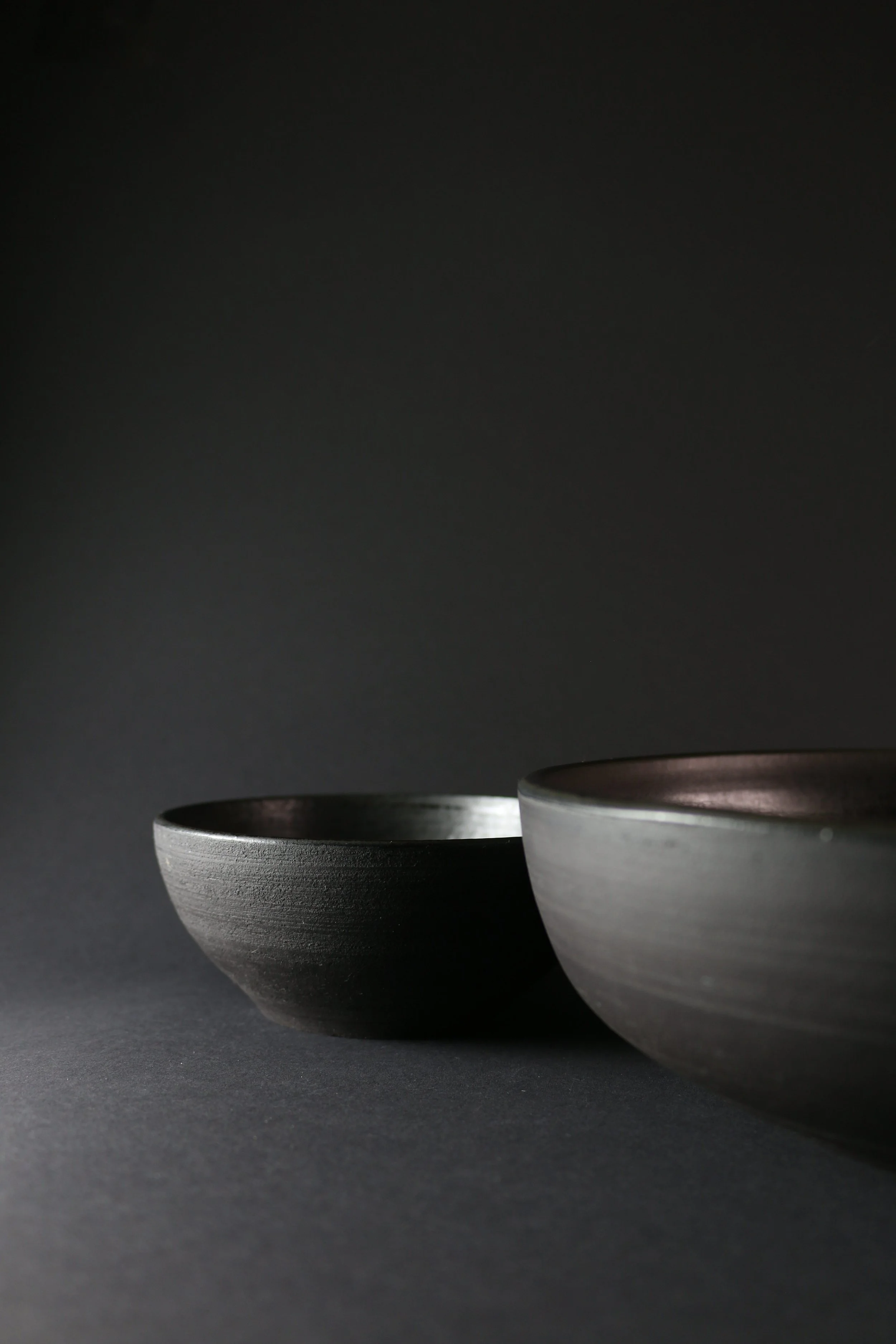 Two black and gray ceramic bowls placed on a dark surface against a dark background.