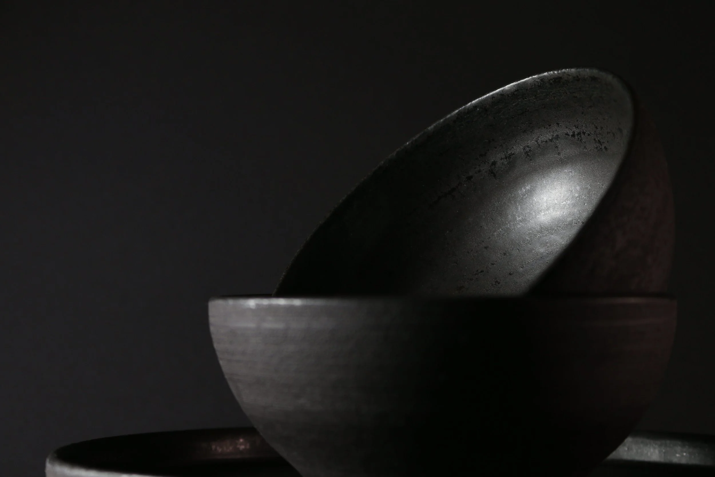 Close-up of a black ceramic bowl, showing glaze details, against a dark background.