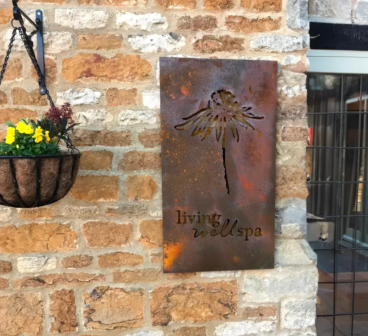 Bespoke Corten steel Living Well Spa sign mounted on a rustic stone wall at Homefield Grange, connecting the spa’s branding with its farmhouse heritage.