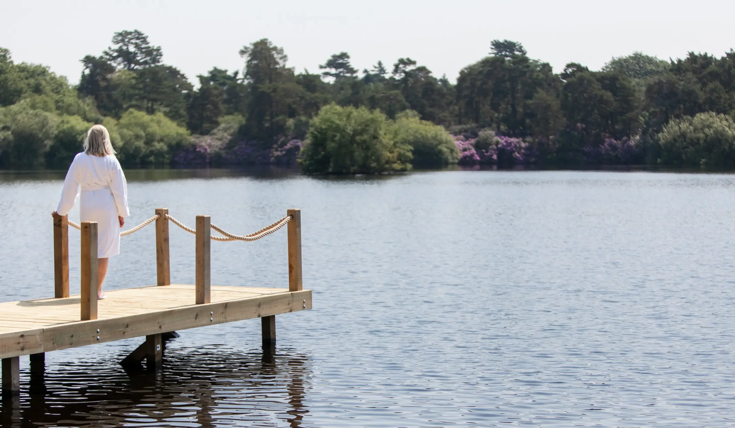 A woman overlooking the lakes at Champneys Forest Mere after using the thermal suite helping to connect with nature.
