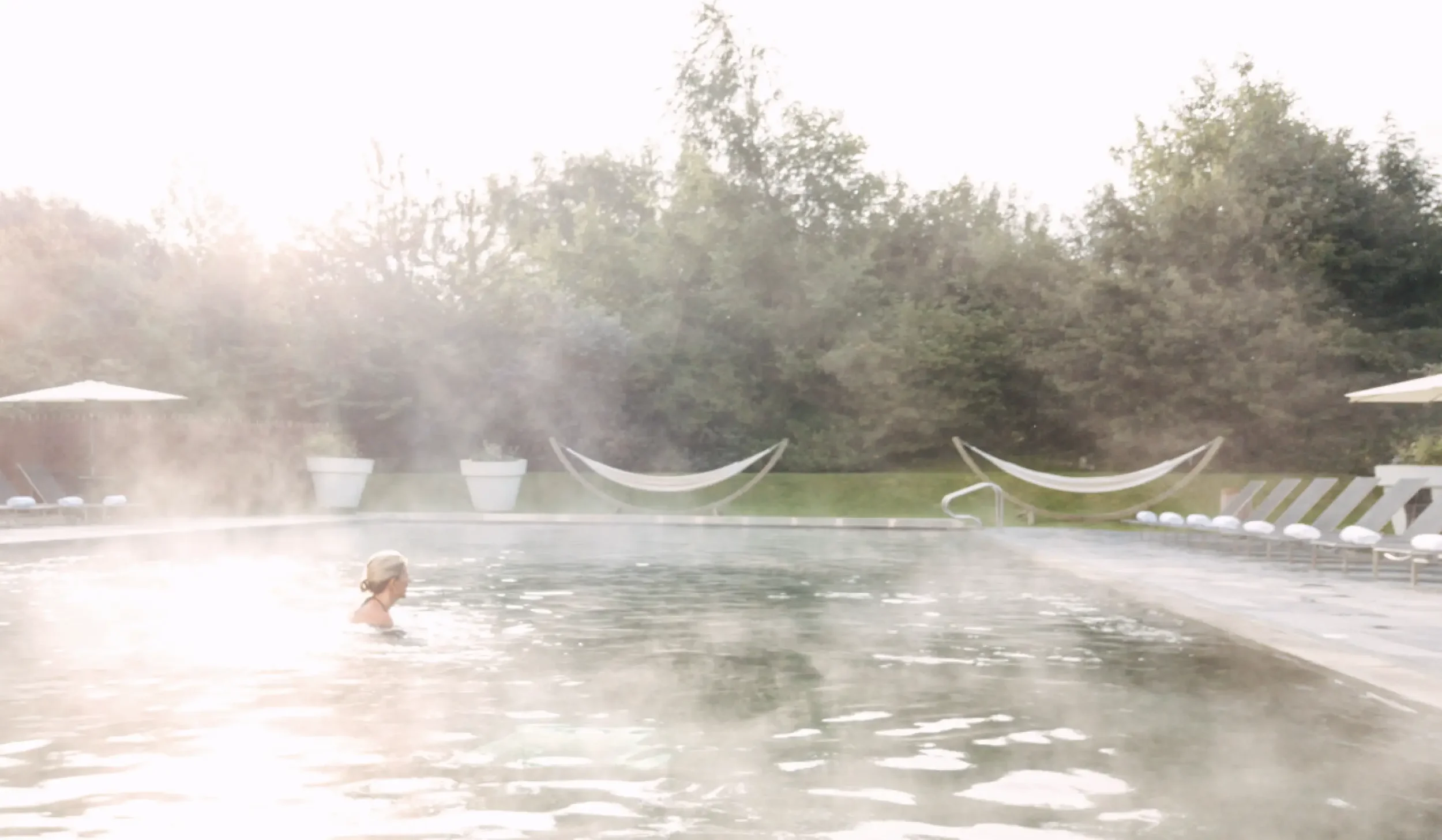 Steaming outdoor pool at Lower Mill Estate Spa surrounded by woodland in the early morning.