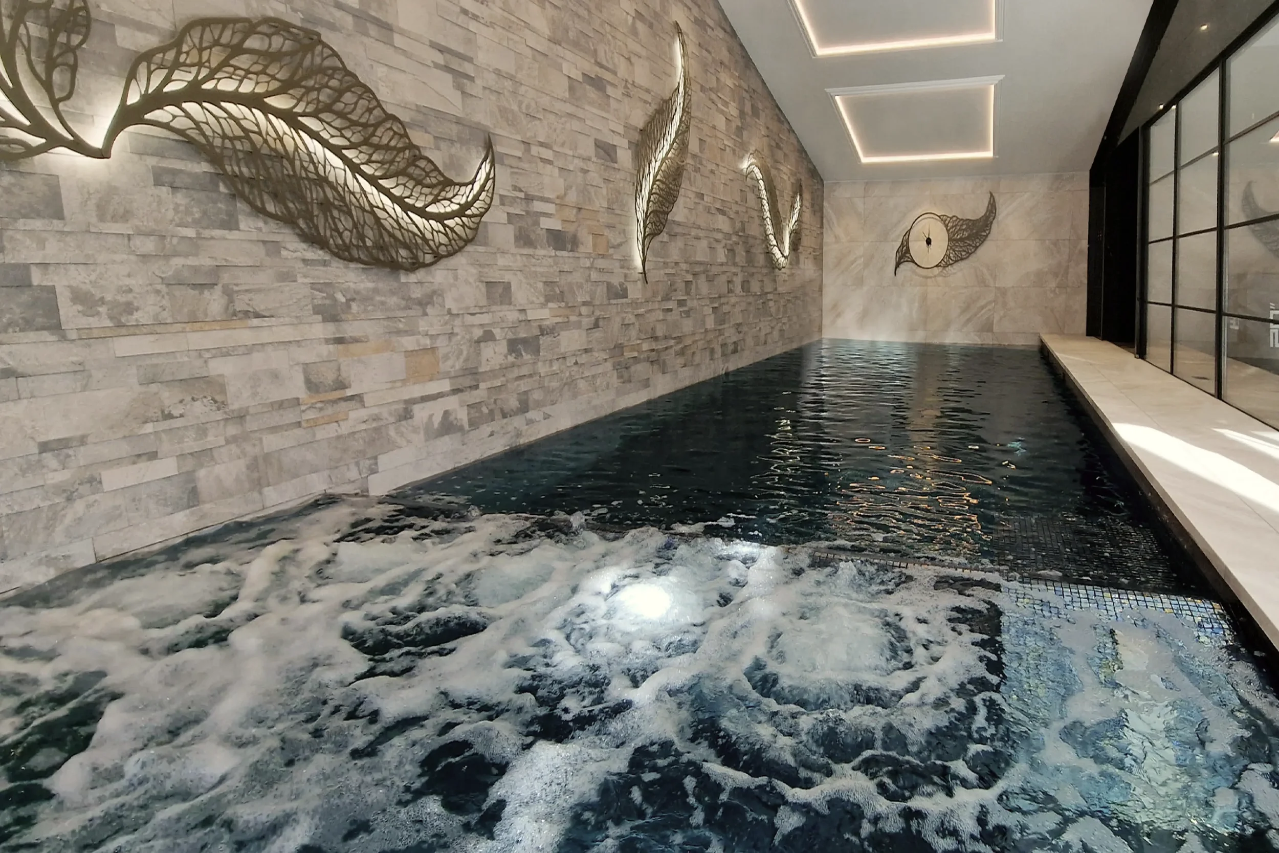 Luxury private spa and hydrotherapy pool in a New Forest residence, featuring deep blue mosaic tiles, bespoke illuminated artwork and natural stone walls.