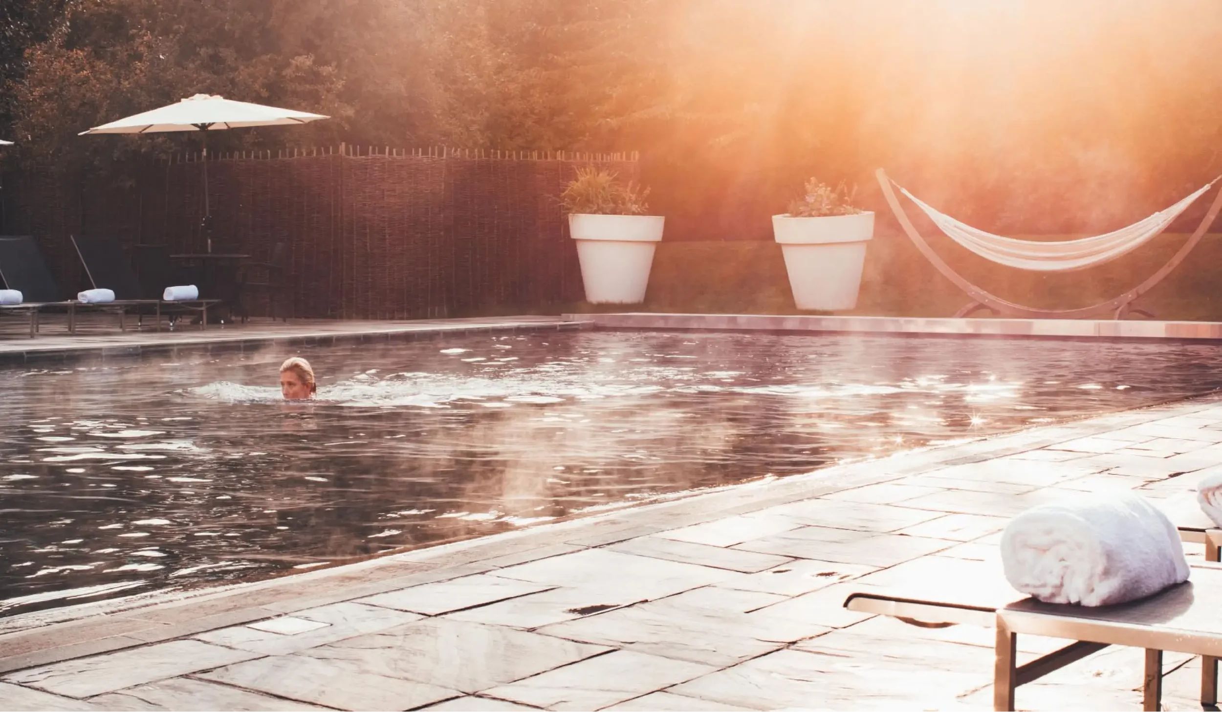 Guest swimming in the outdoor pool at Lower Mill Estate Spa with warm evening light across the water.