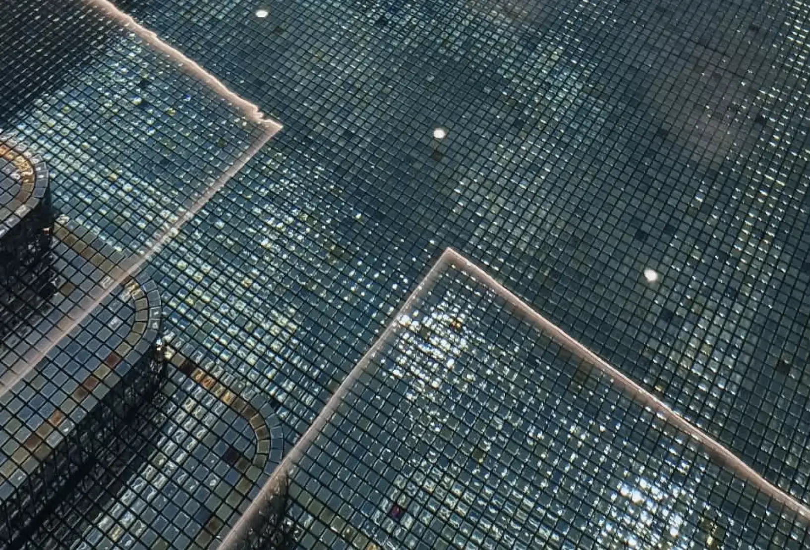 Close-up of rich turquoise-blue mosaic tiles lining the indoor swimming pool and submerged steps, creating depth and shimmering reflections in the water.