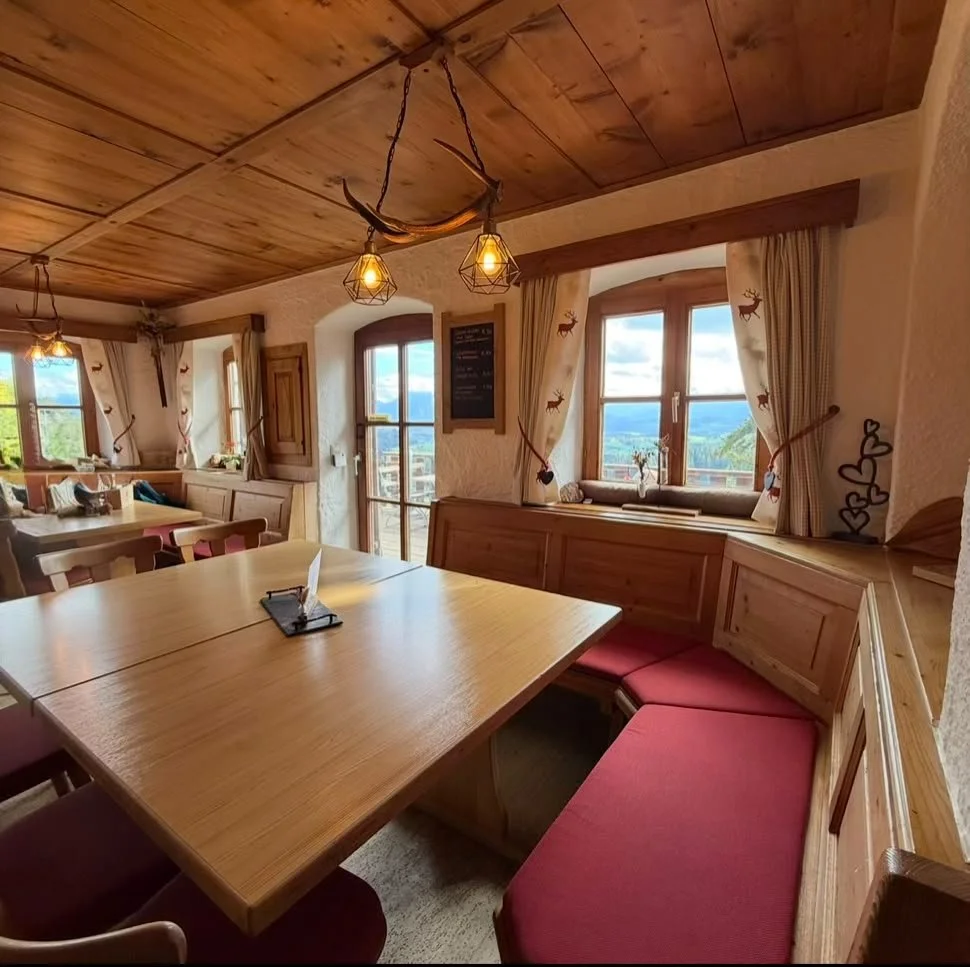 Gemütliche Stube der Alpe Beichelstein mit Holztischen, roten Sitzbänken und Panoramablick auf das Ostallgäu.