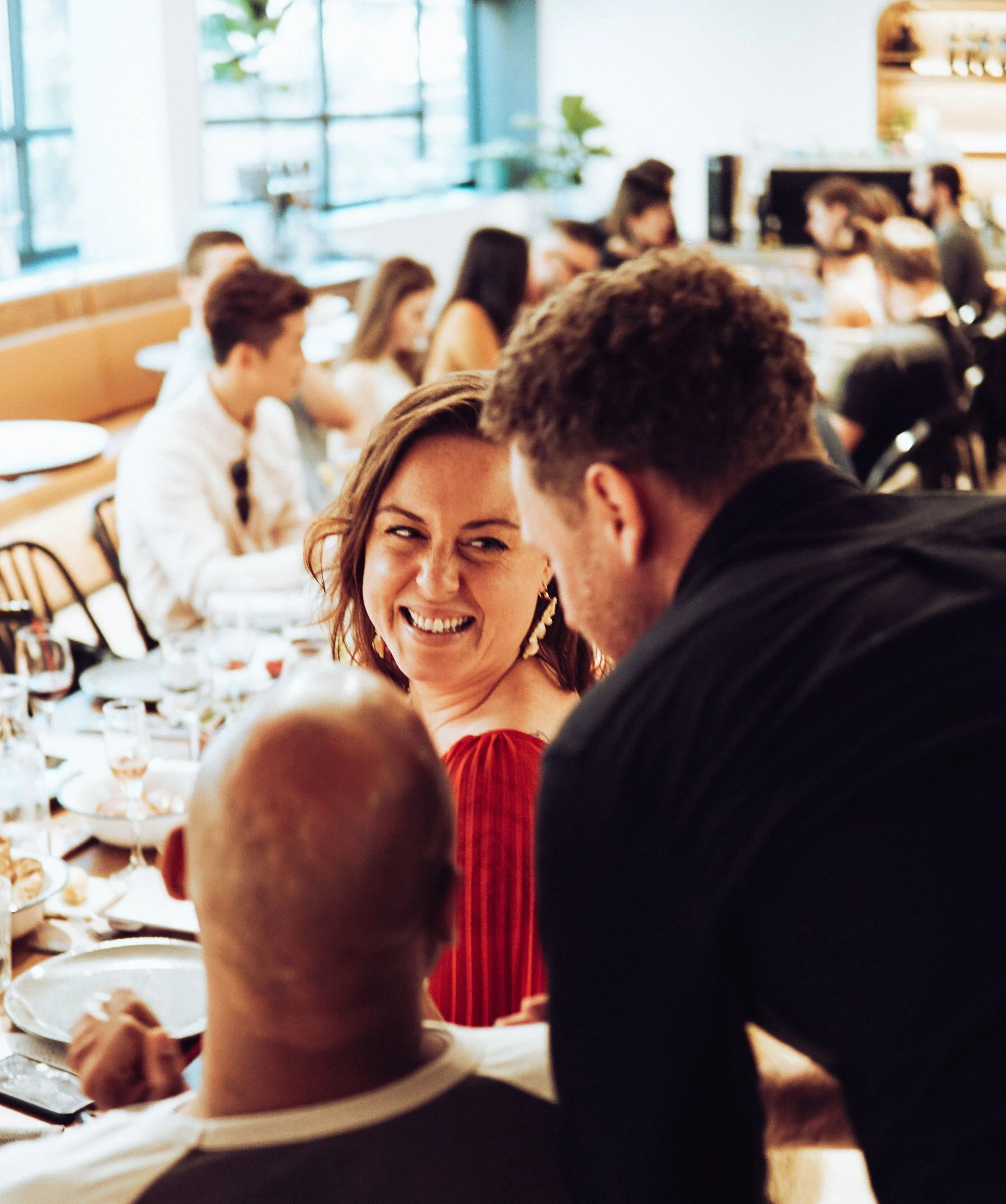 People gathered around a table at a social event, smiling and engaging with each other, with plates and glasses on the table.
