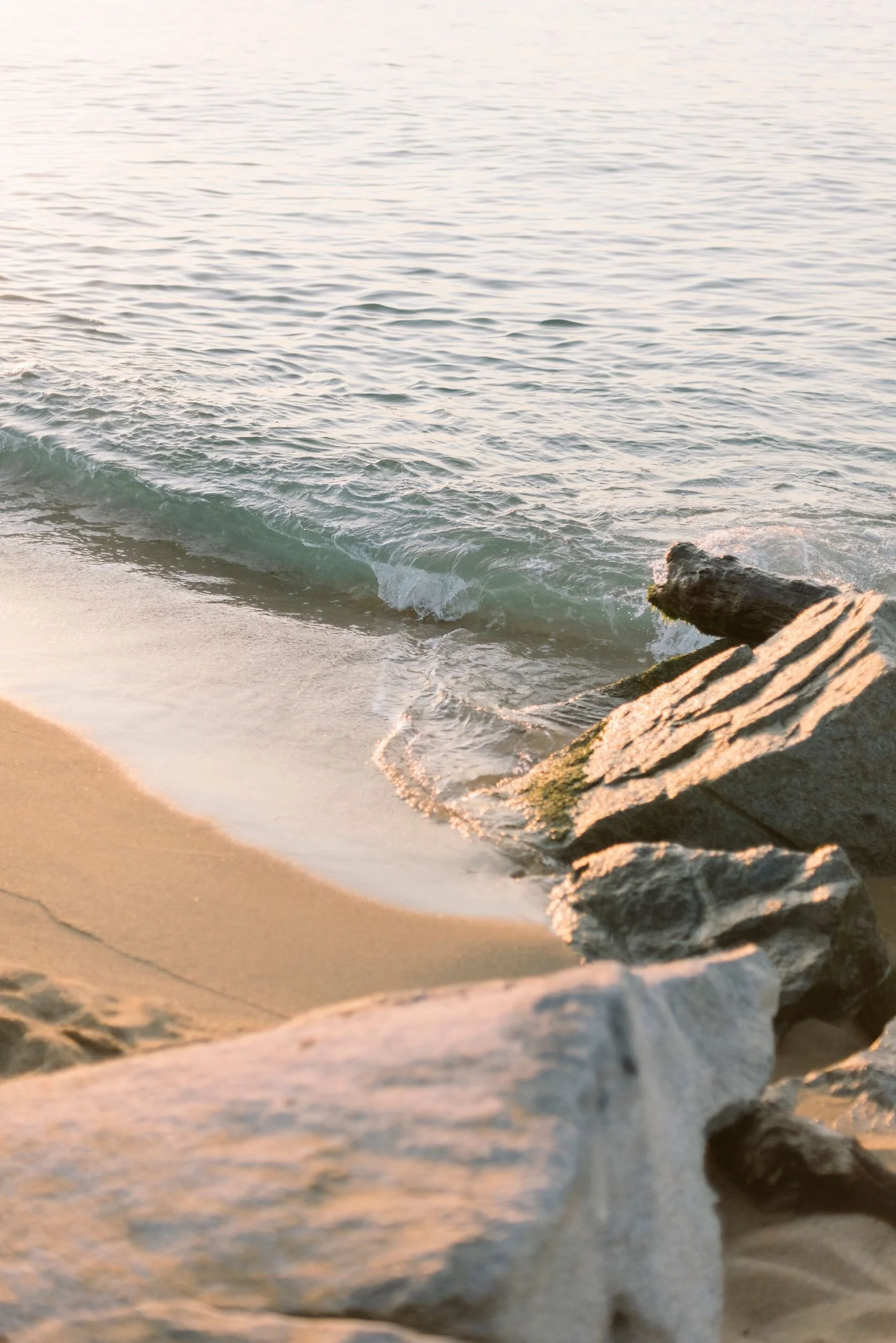 A serene beach scene with gentle waves washing onto the sandy shore, bordered by rocks.