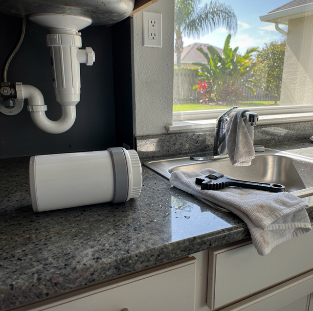 Kitchen sink with plumbing, filter cartridge, brush, and towel on counter near window overlooking yard.