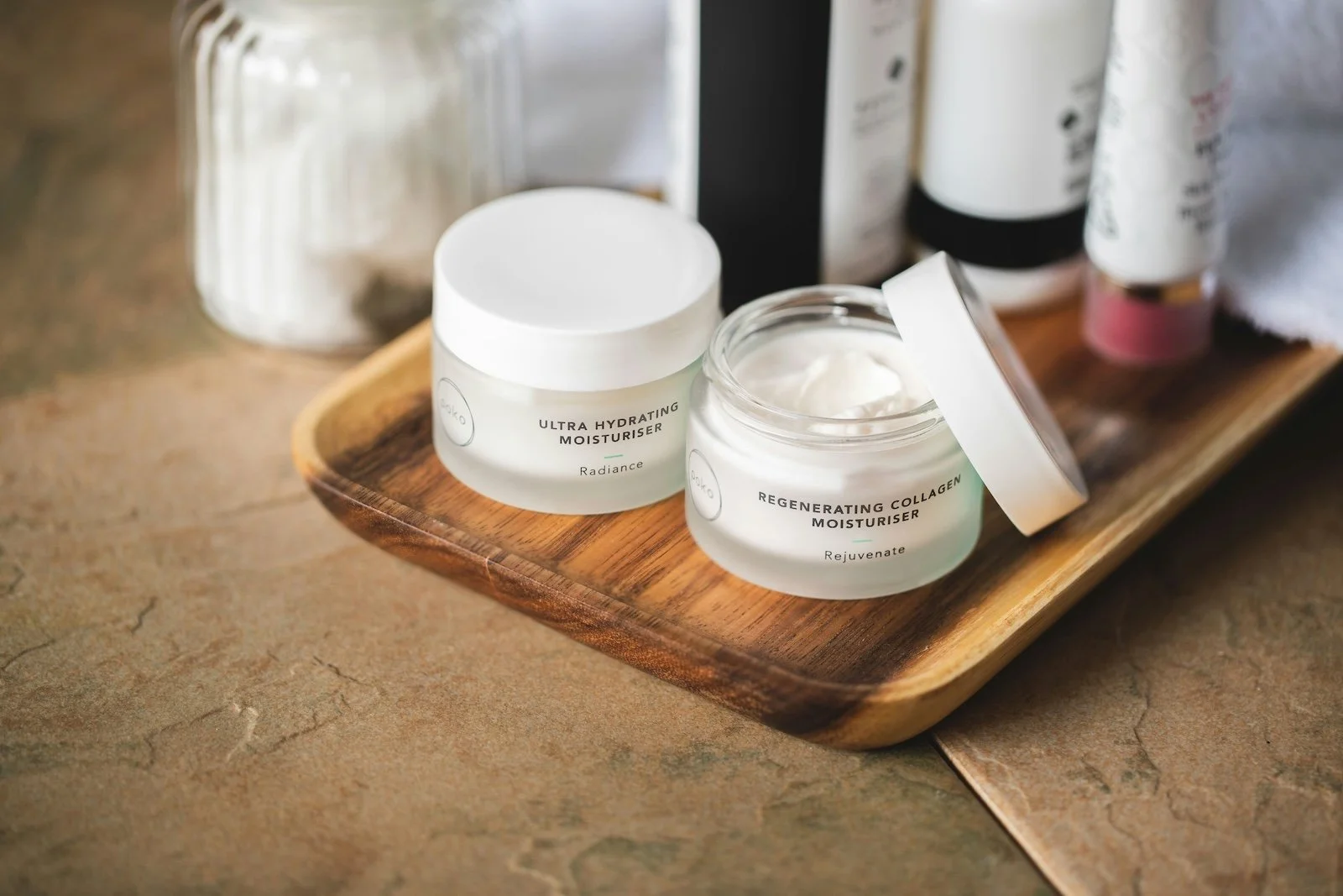 Open jar of regenerating collagen moisturizer and a closed jar of ultra hydrating moisturizer on a wooden tray.