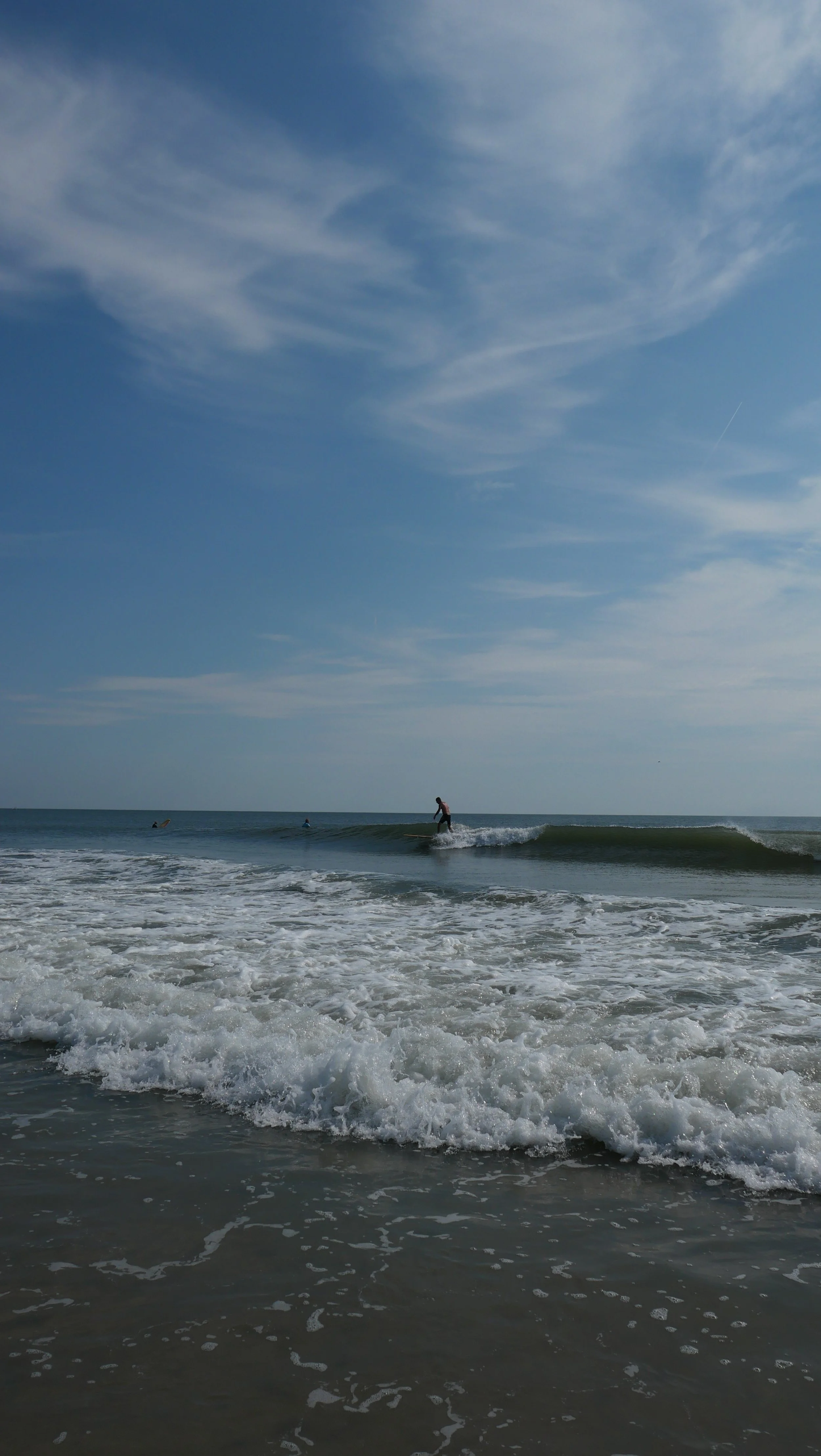 People surfing in the ocean waves under a partly cloudy sky.