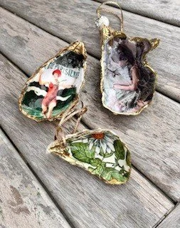 Three decorated seashell ornaments with string hangers, placed on a wooden surface.