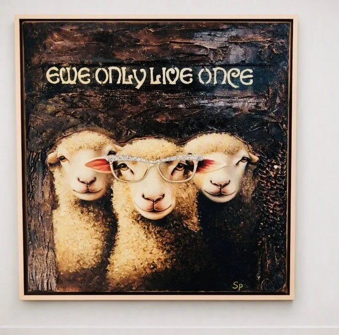 A painting of three sheep with glasses, accompanied by the phrase 'Ewe Only Love Once' written above them.