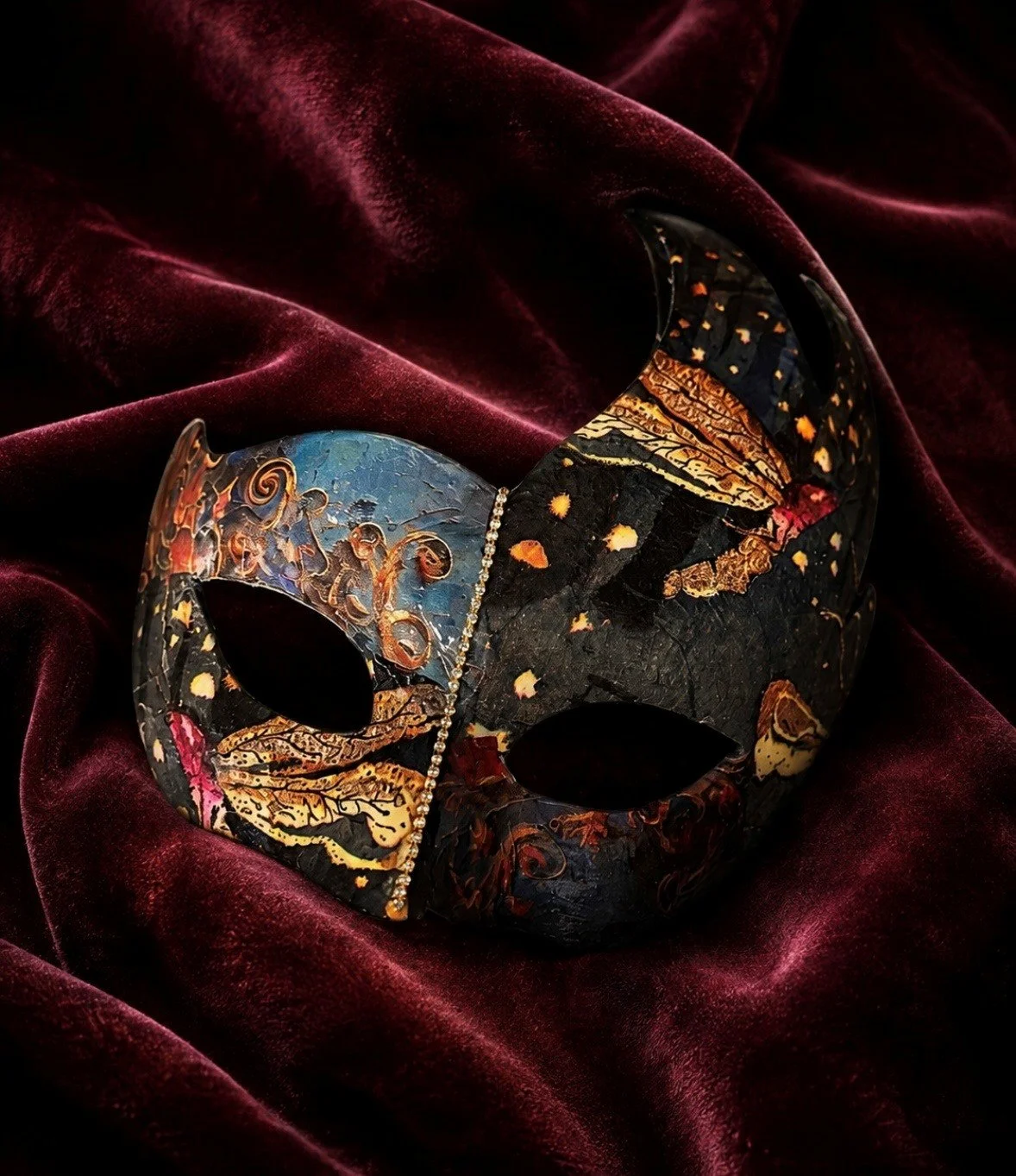 A decorative Venetian-style mask with intricate painted designs, resting on red velvet fabric.
