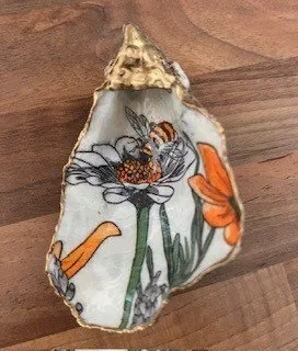 Decorative ceramic seashell with painted flowers and a bee on a wooden surface.