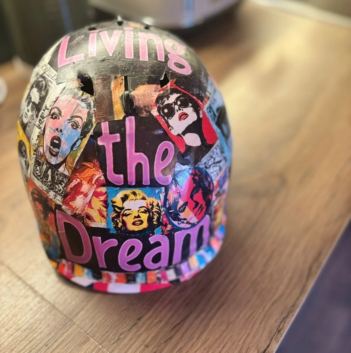A colorful helmet decorated with collage stickers that include pop art images and the phrase "Living the Dream."