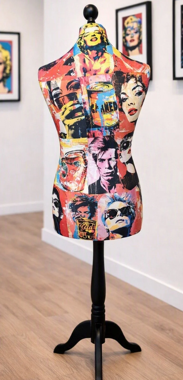 A mannequin torso covered in colorful pop art images of various women's faces and cans, displayed on a black stand.
