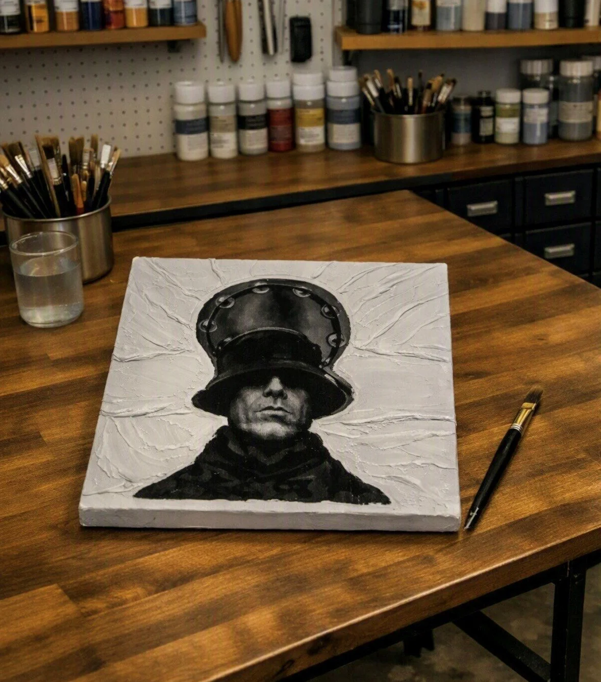 A painting of a woman with a large hat featuring a circular design, displayed on a wooden table in an art studio.