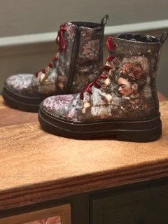 A pair of children's boots decorated with images of a woman and floral patterns, placed on a wooden surface.