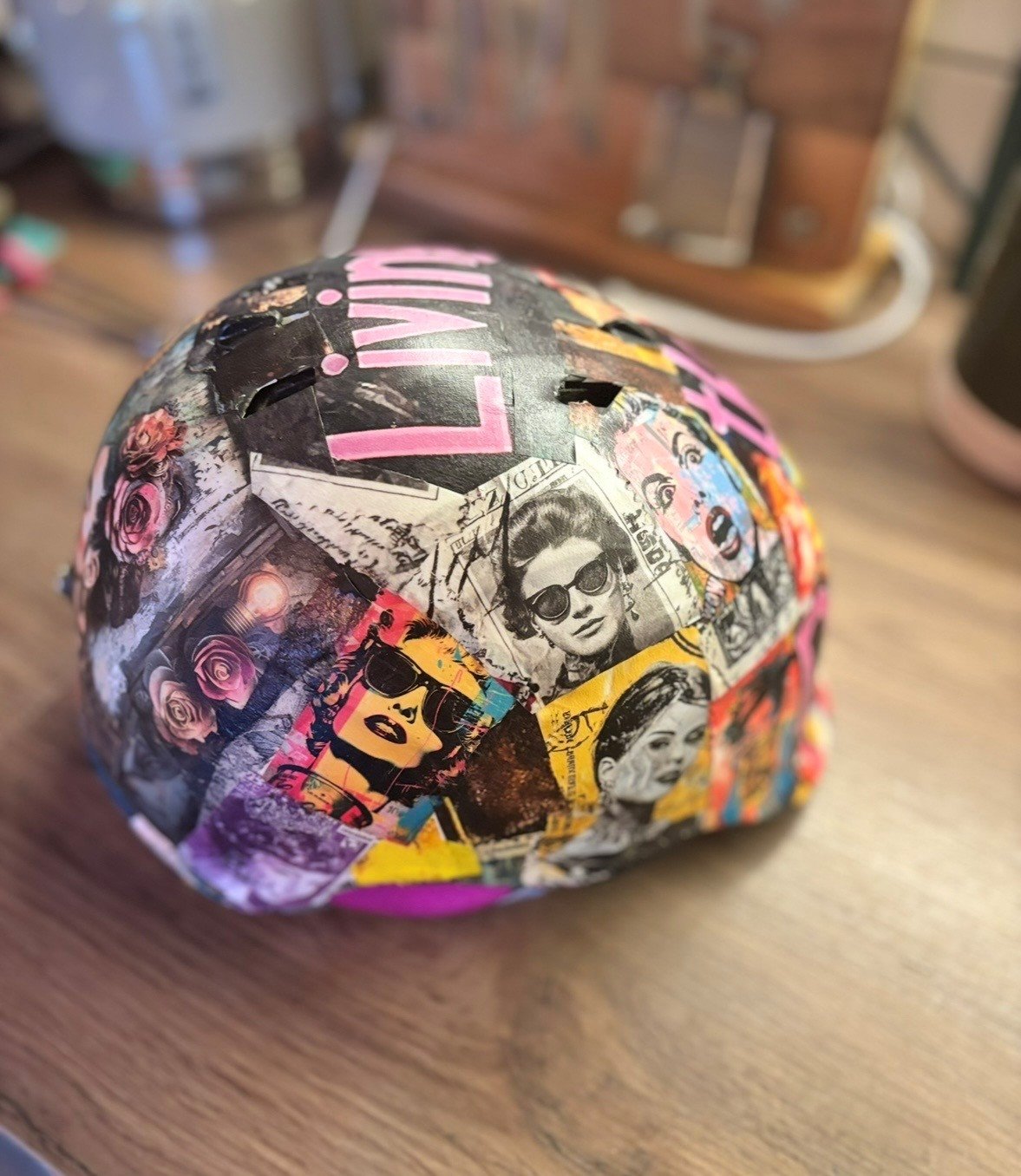 A spherical object decorated with a collage of vintage comic book-style images of women in sunglasses and flowers, placed on a wooden surface.