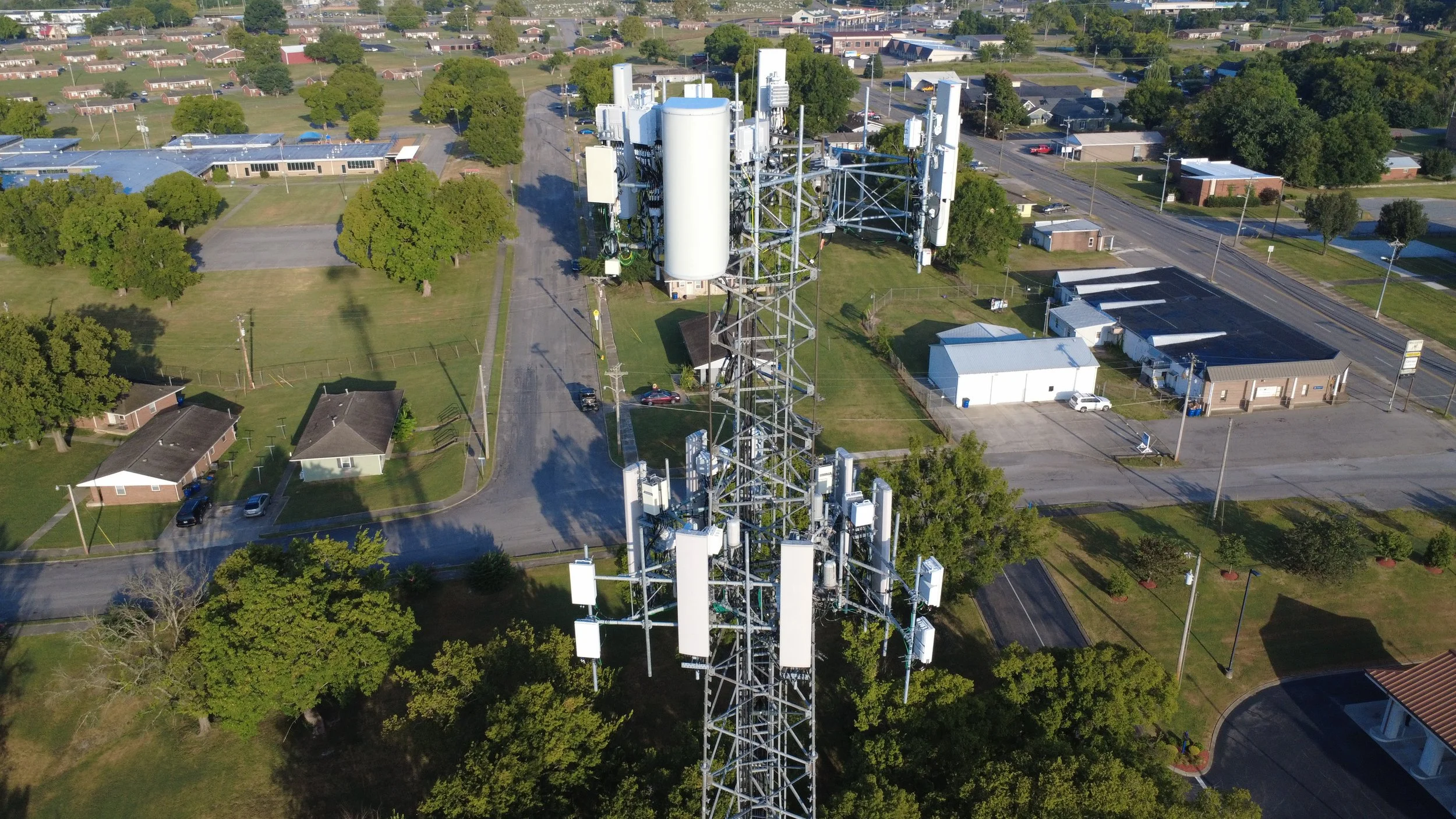 Aerial view of a communication tower surrounded by residential buildings, roads, and green trees in a suburban area.