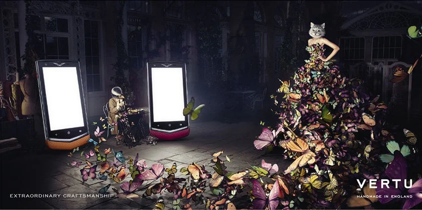 Fashion show featuring a model with a cat mask and a dress made of colorful butterflies, flanked by two large mobile phone screens displaying blank white screens.
