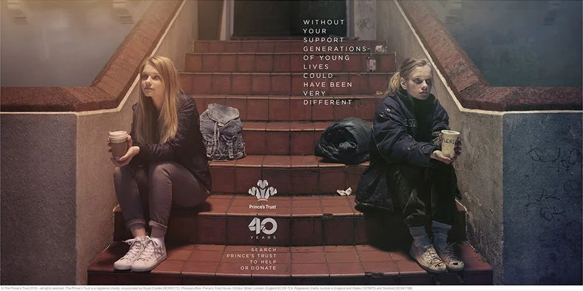 Two young women sitting on outdoor stairs, one holding a coffee cup and the other holding a book, with supporting text about generational support and charity.