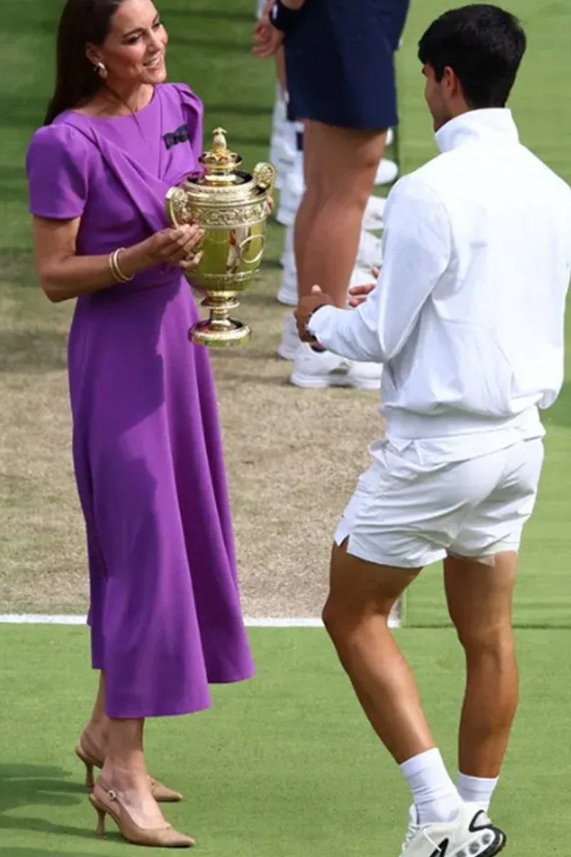 Queen Elizabeth II presenting a trophy to a man dressed in tennis attire on a tennis court.