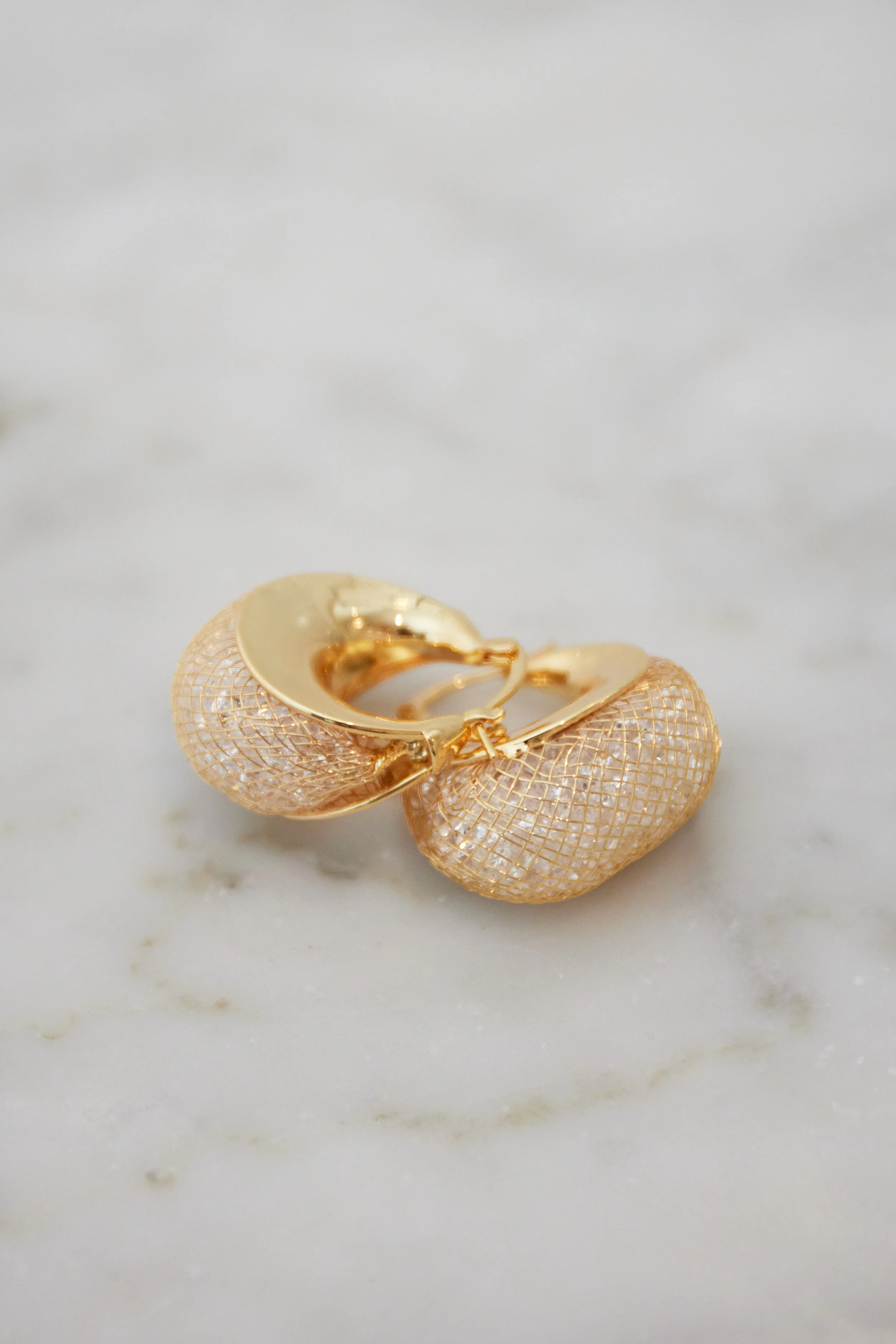 Close-up of a gold mesh ring holder with a gold ring on it, placed on a white marble surface.
