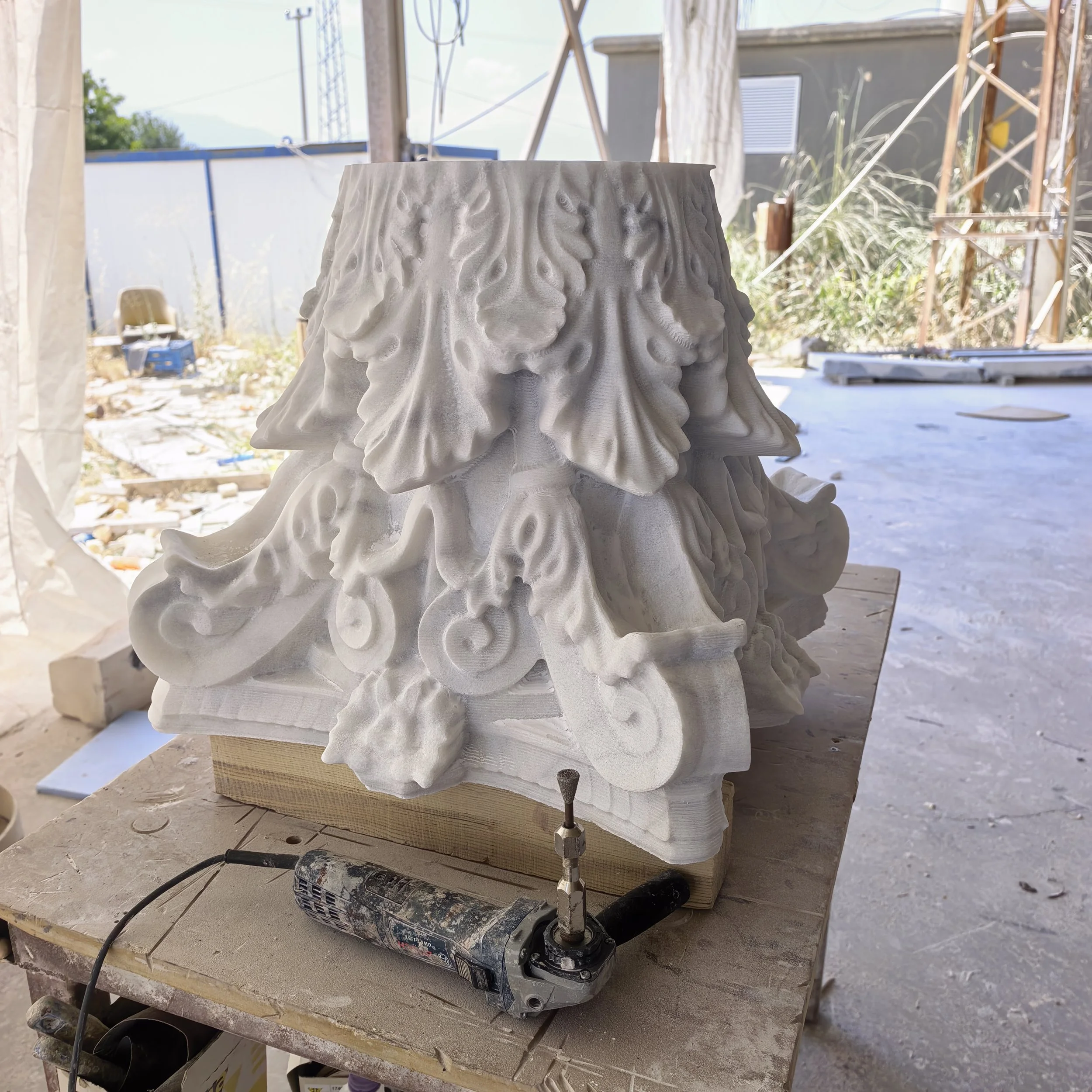 Unfinished hand-carved stone sculpture on a worktable with carving tools outdoors.