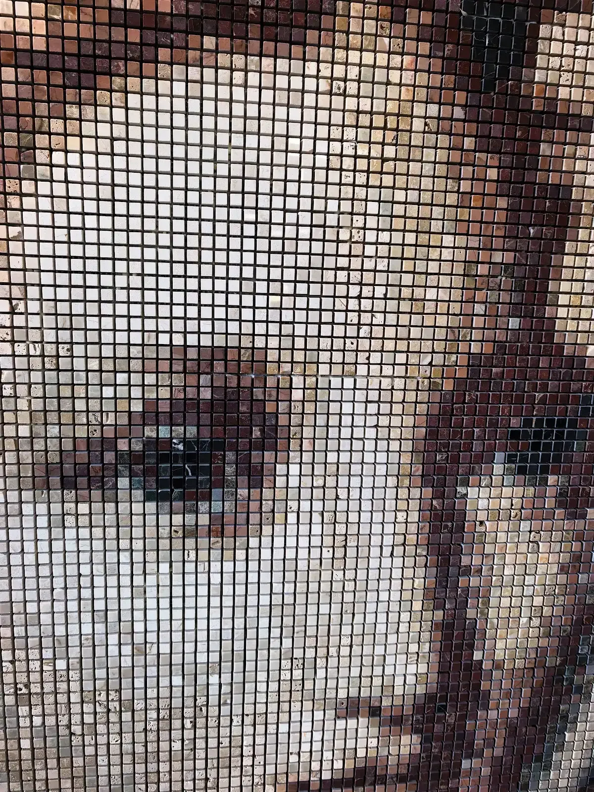 Detail of a stone mosaic portrait, showing individual marble tesserae forming a face in warm brown and cream tones