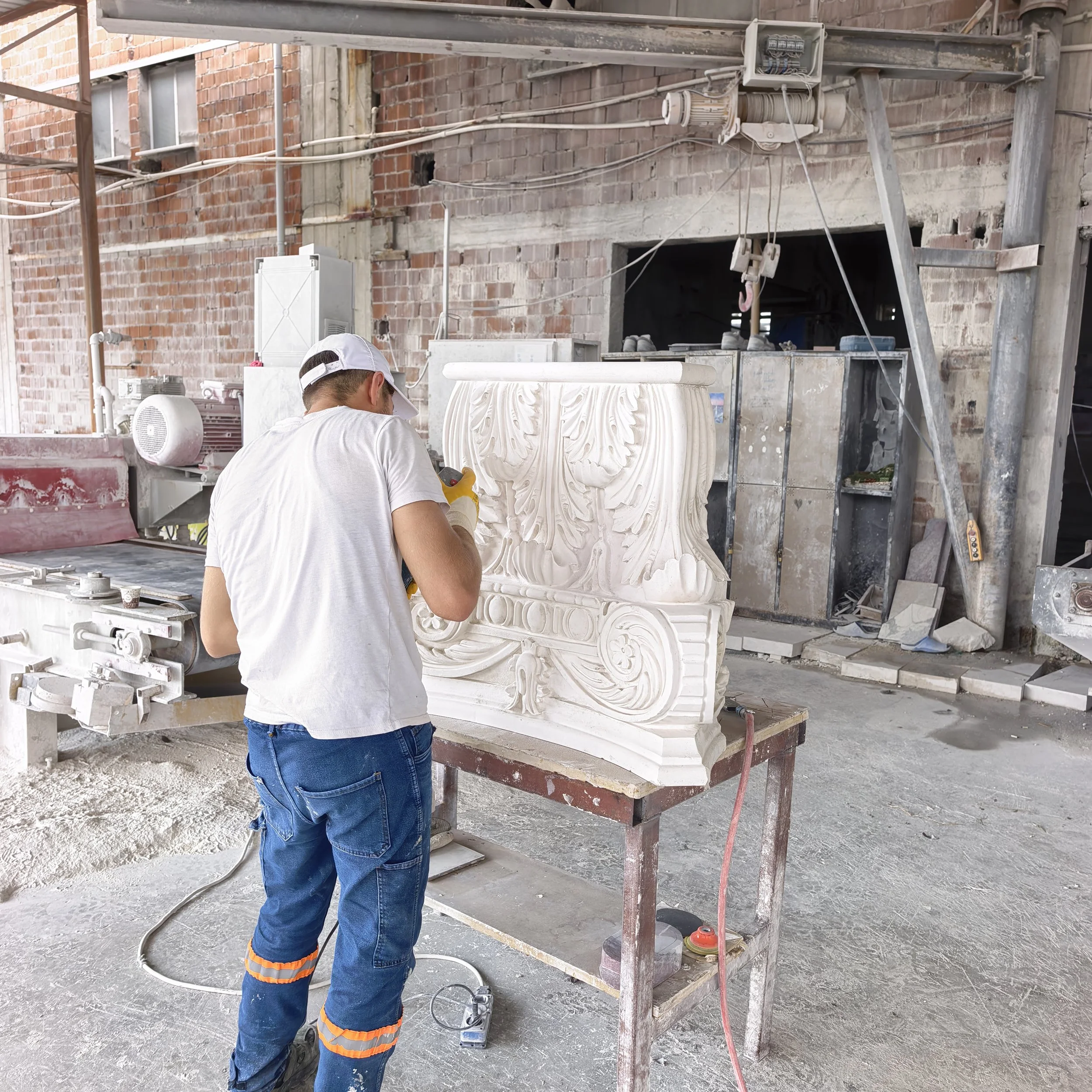 Worker finishing a decorative carved stone pedestal at an indoor workshop site.