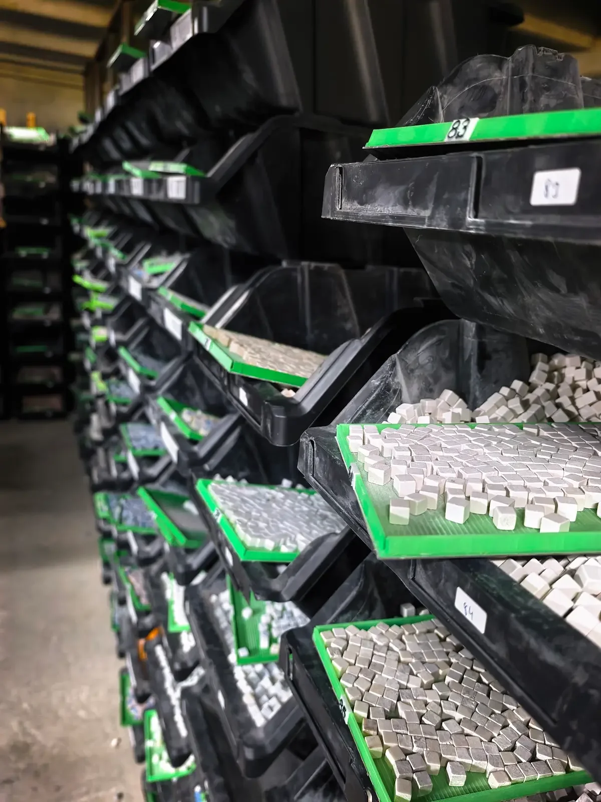 Shelves of bins holding sorted natural stone tesserae in marble and travertine tones
