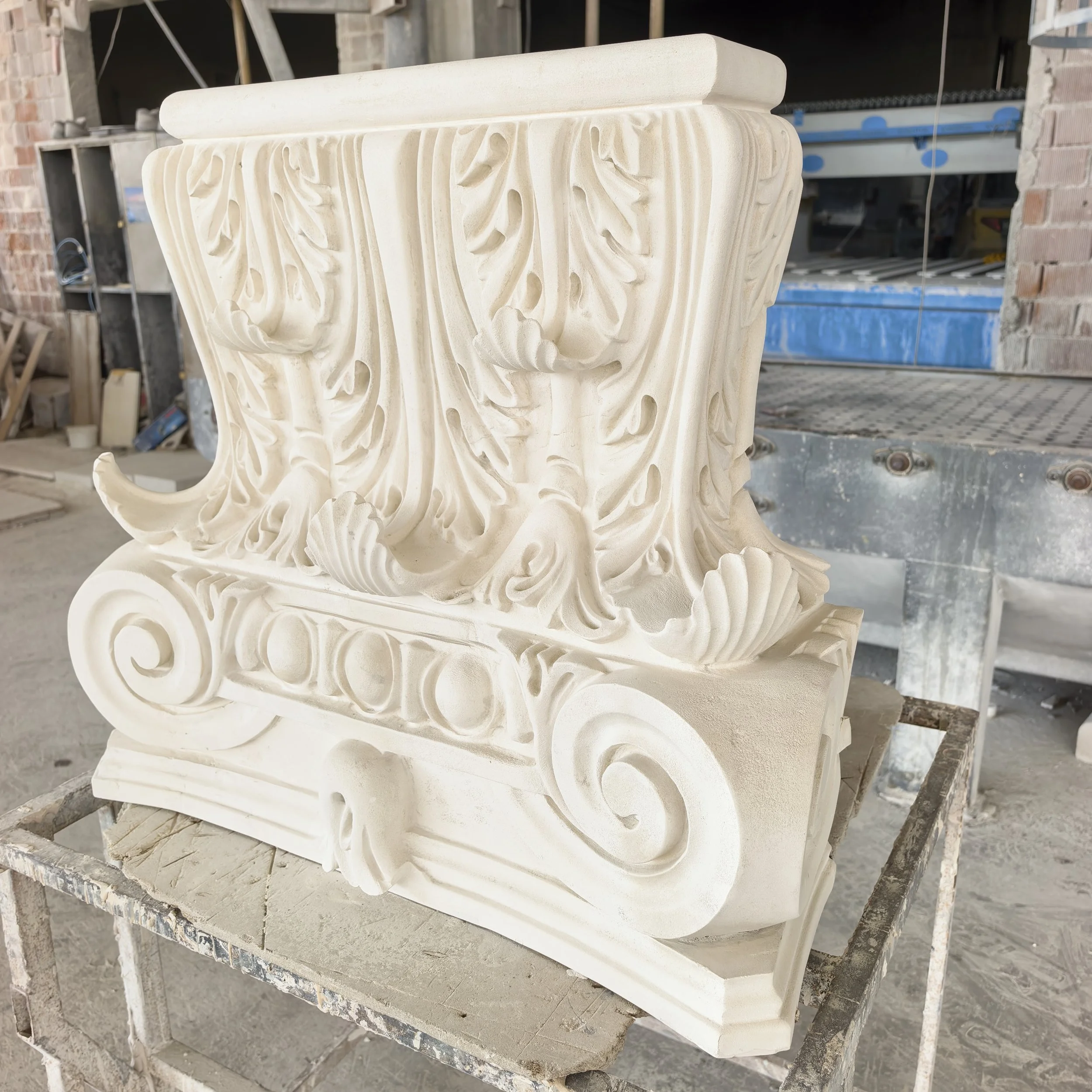 Ornate hand-carved marble pedestal with intricate floral patterns in a workshop.
