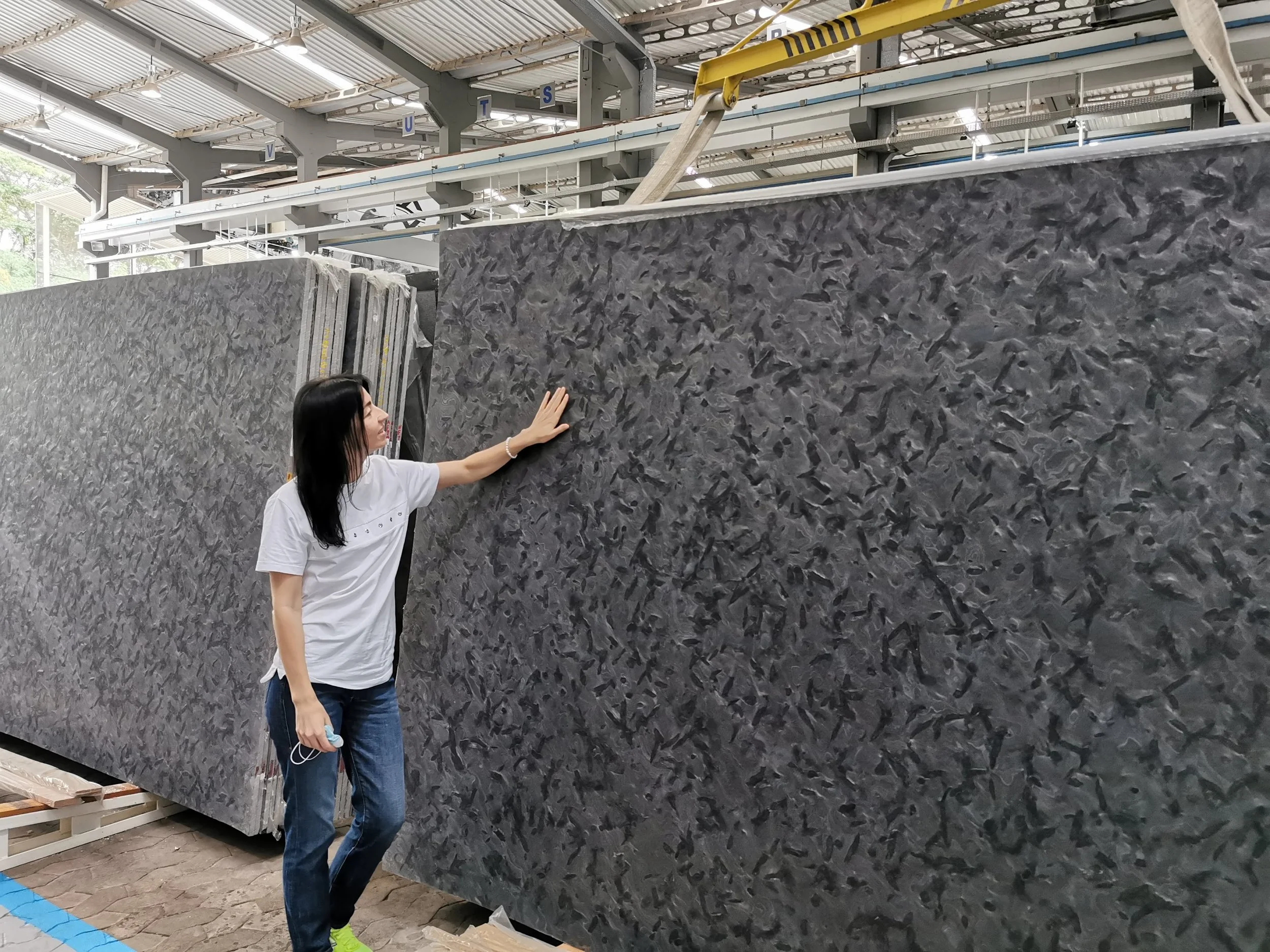 Woman examining a large dark gray marble slab in a stone showroom.