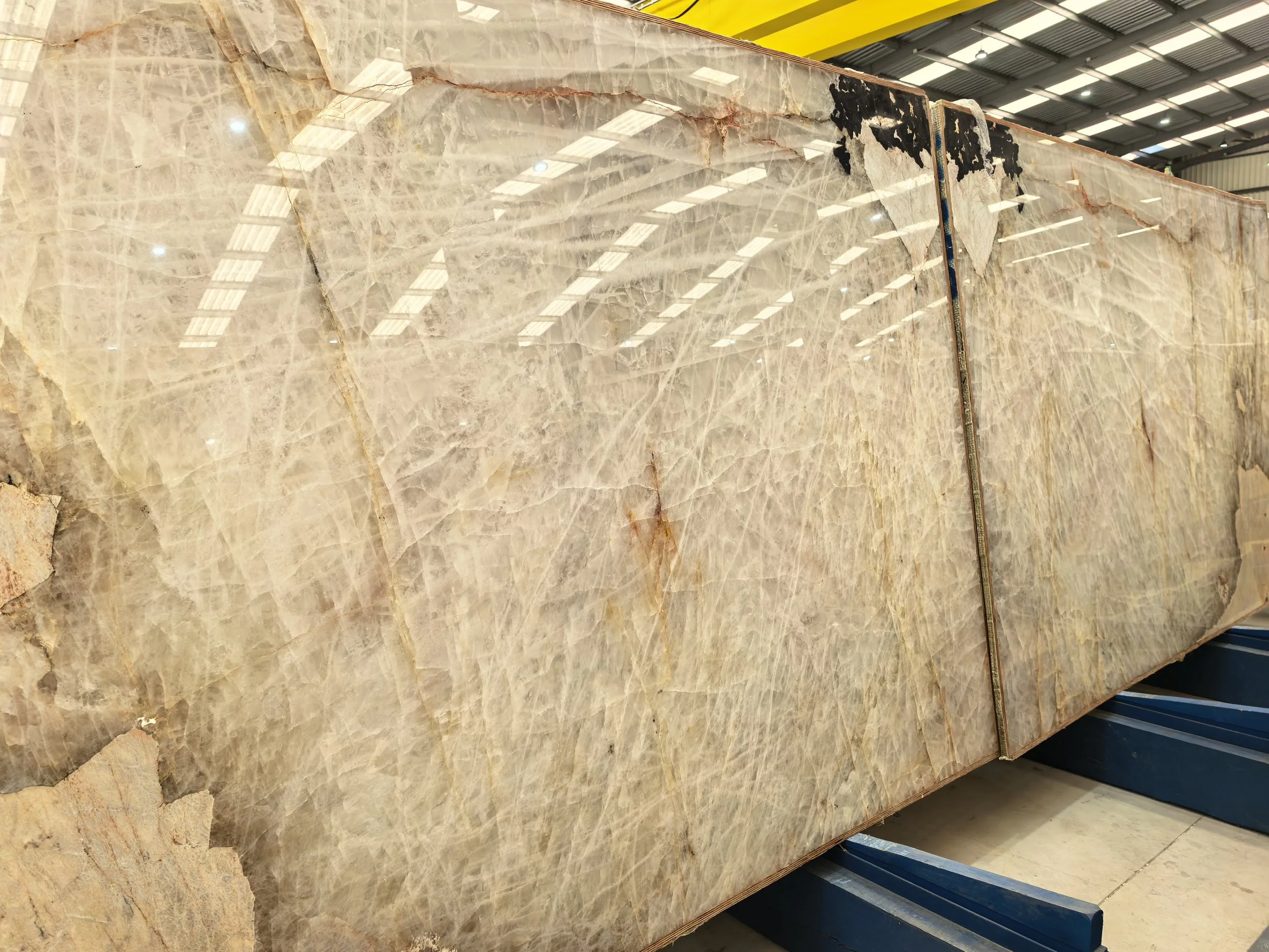 Large beige marble slab with natural veining on display in a warehouse.